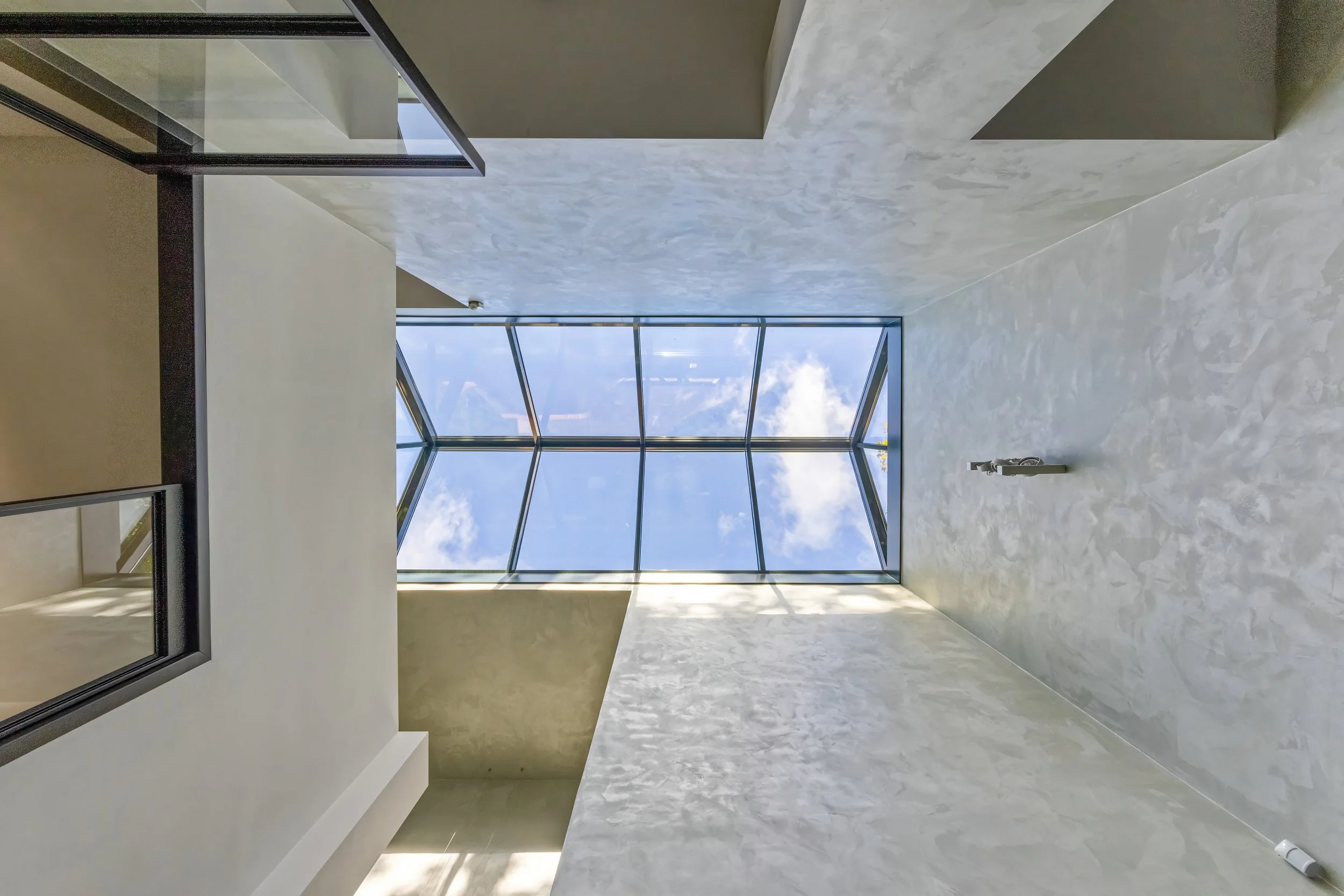 Interieur van een modern gebouw met grote glazen dakraam en lichte muren.