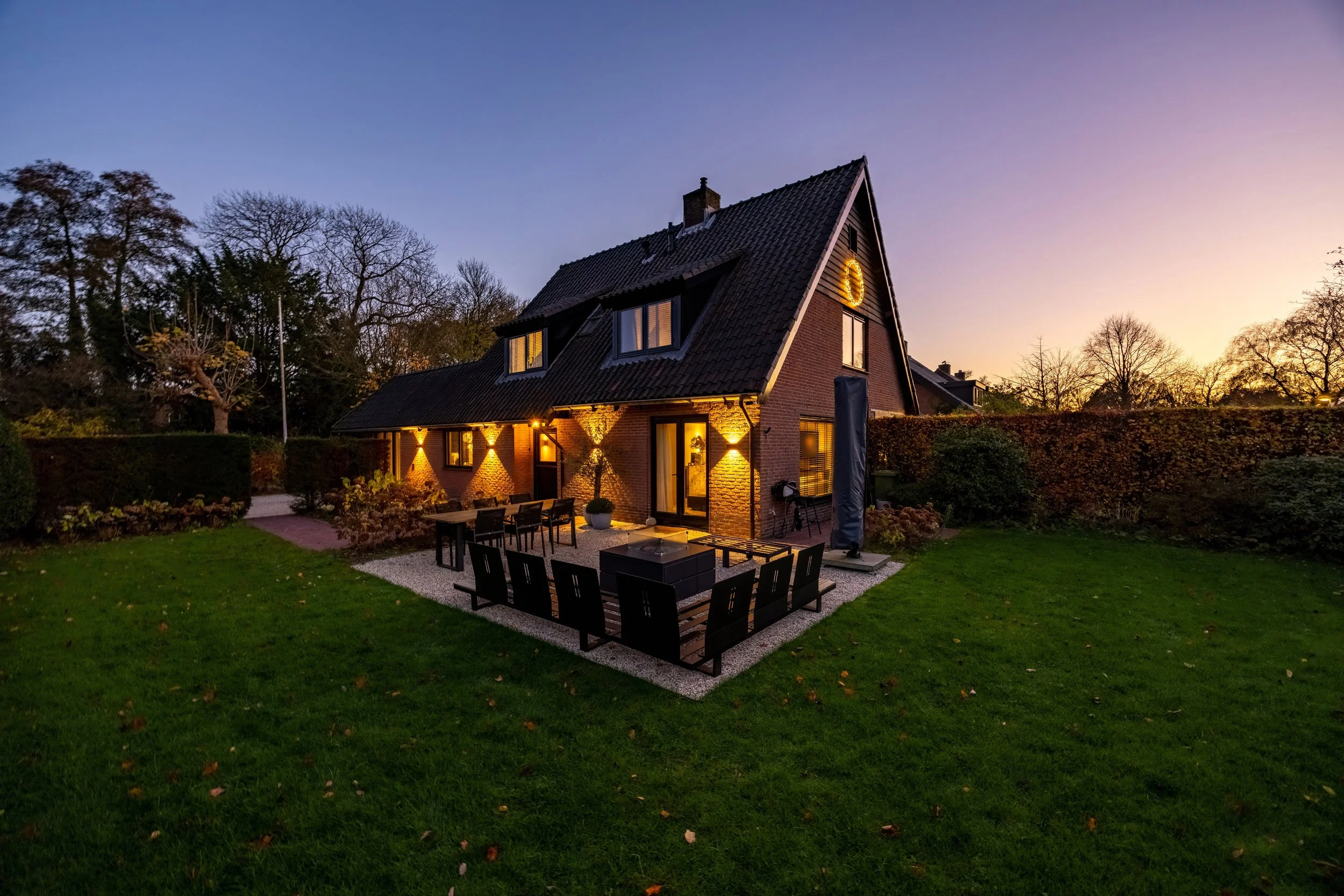 Modern huis met tuin en veranda bij zonsondergang.