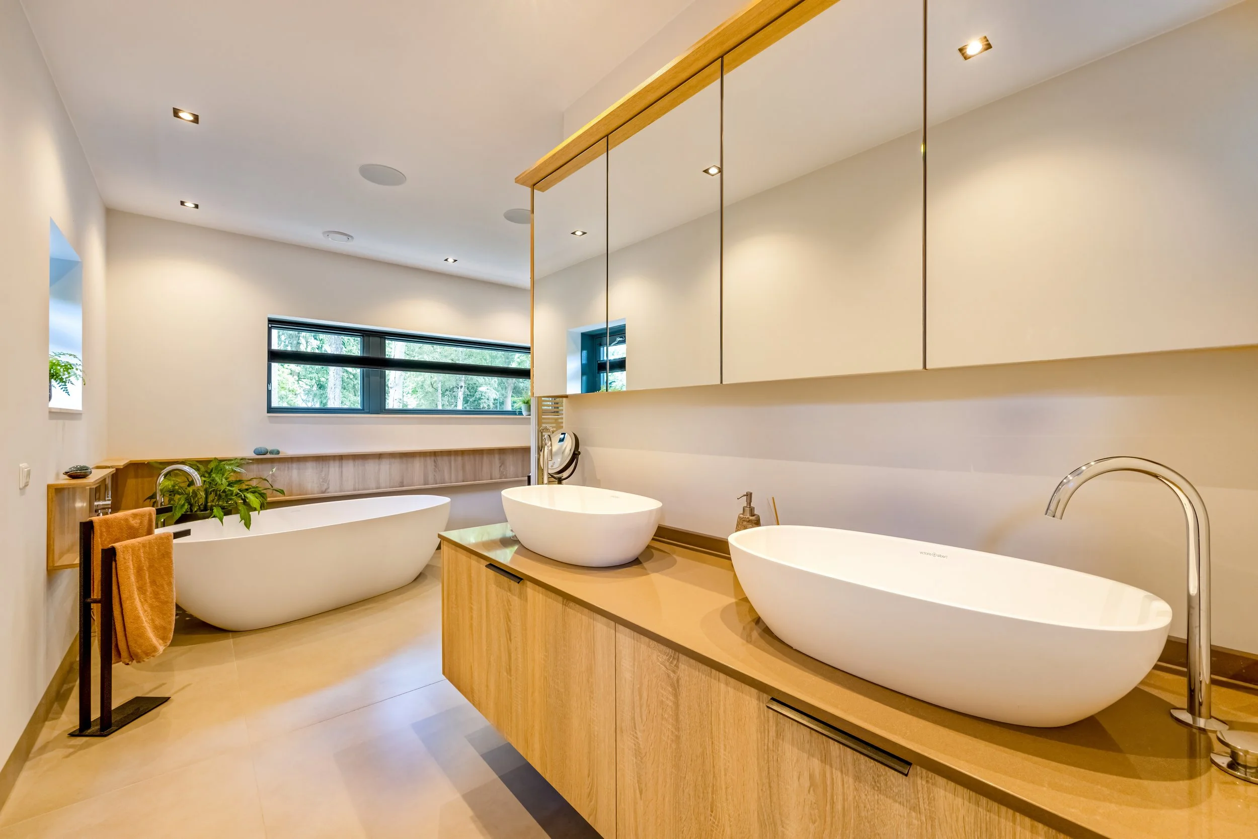 Een moderne badkamer met dubbele wasbakken, een vrijstaande bad en een grote spiegel.