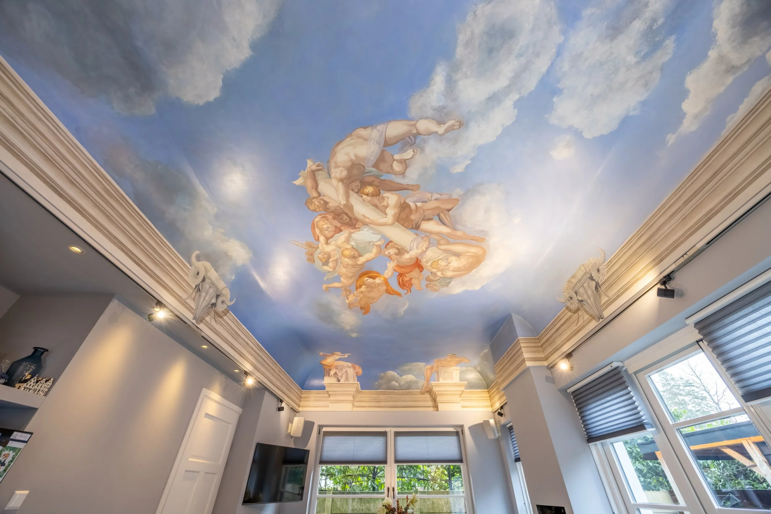 Een kamer met een plafondmuur geschilderd als een hemel met wolken en mythologische figuren.