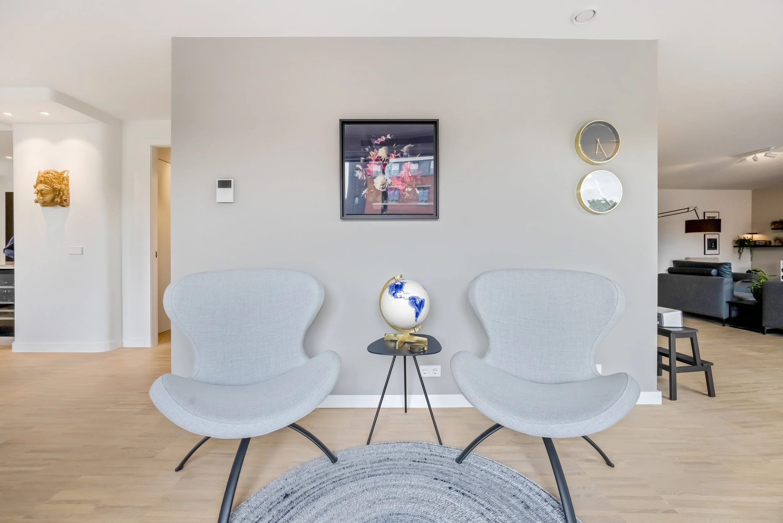Twee witte moderne lounge stoelen met een wereldbol tussen hen op een kleine zwarte tafel in een lichte woonkamer