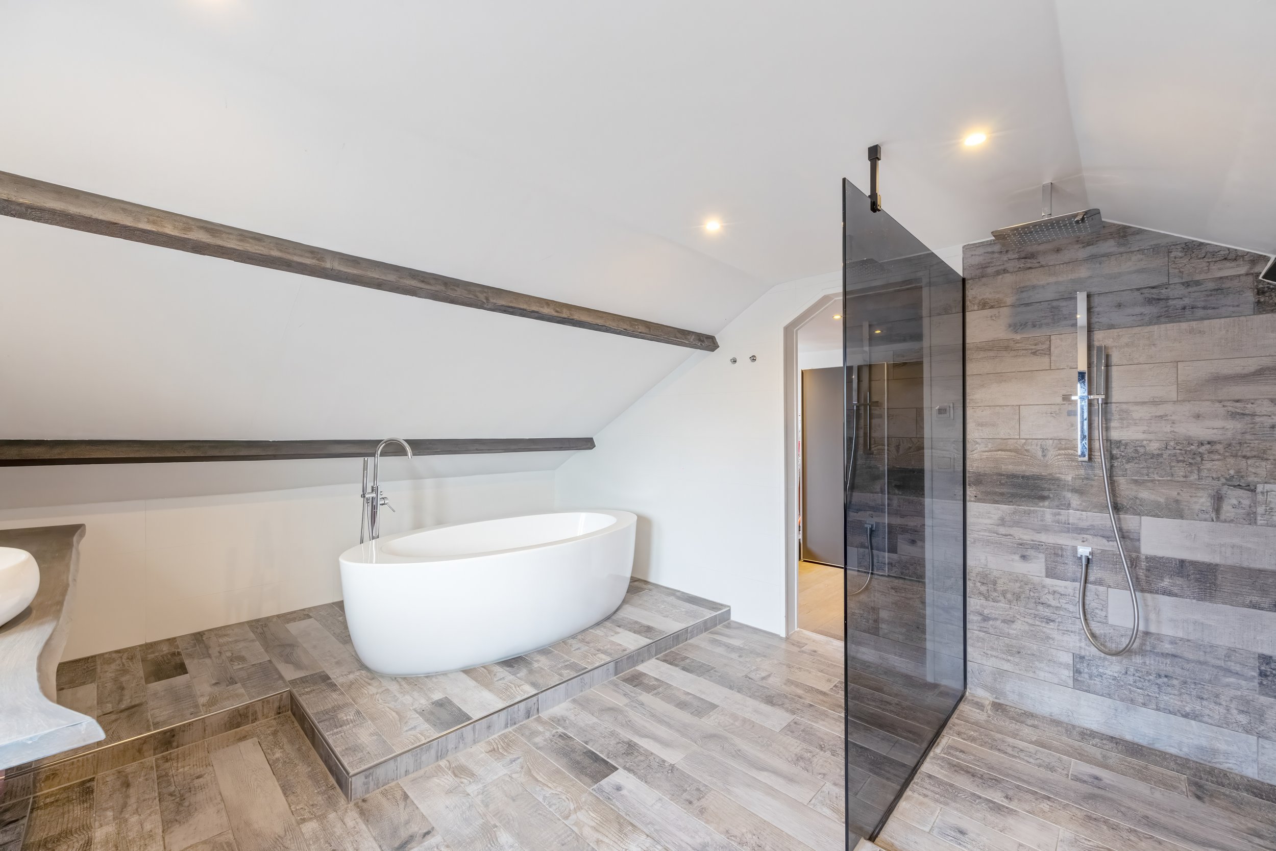 Modern badkamer met witte badkuip, houten vloer en een aparte inloopdouche met glazen wand.
