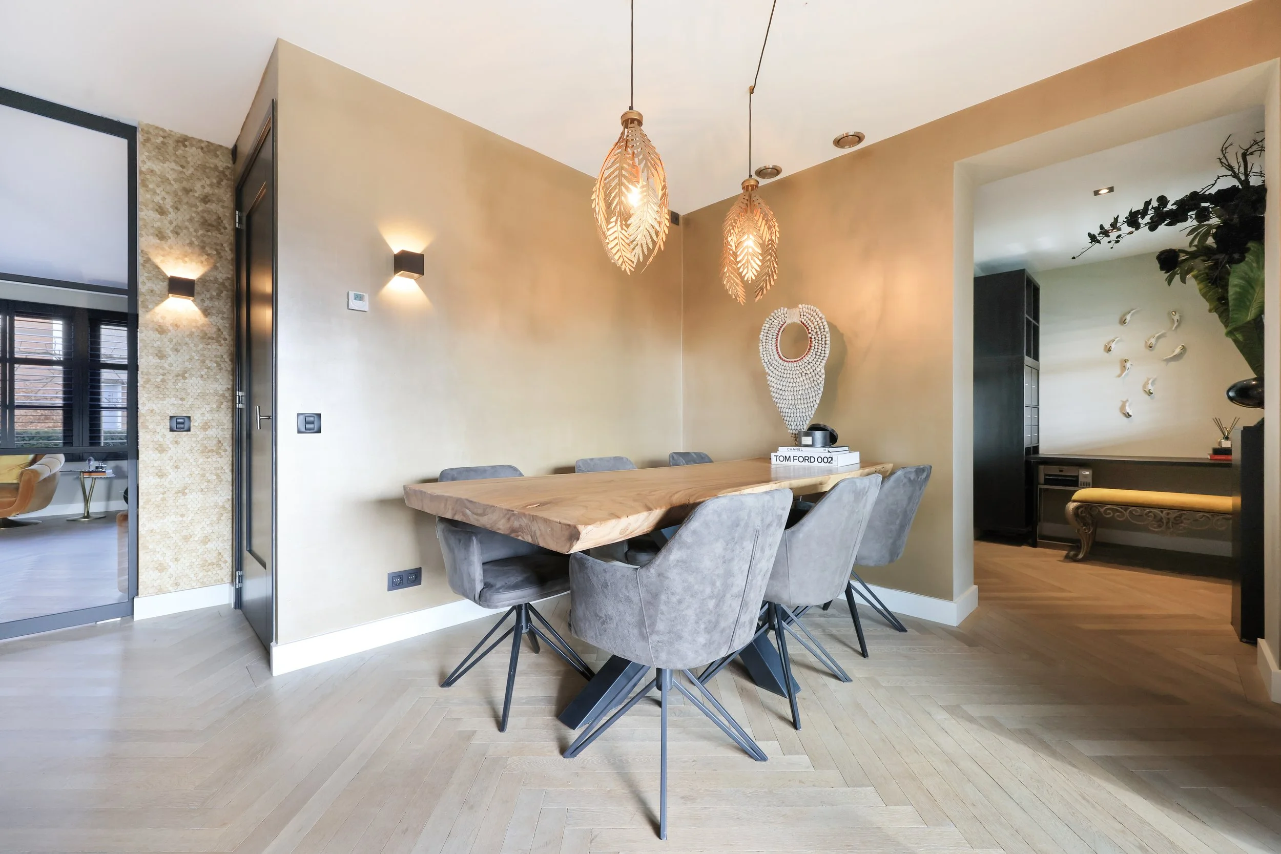 Eettafel met zes grijze stoelen, hanglampen en decoratieve muurversieringen in een modern interieur.