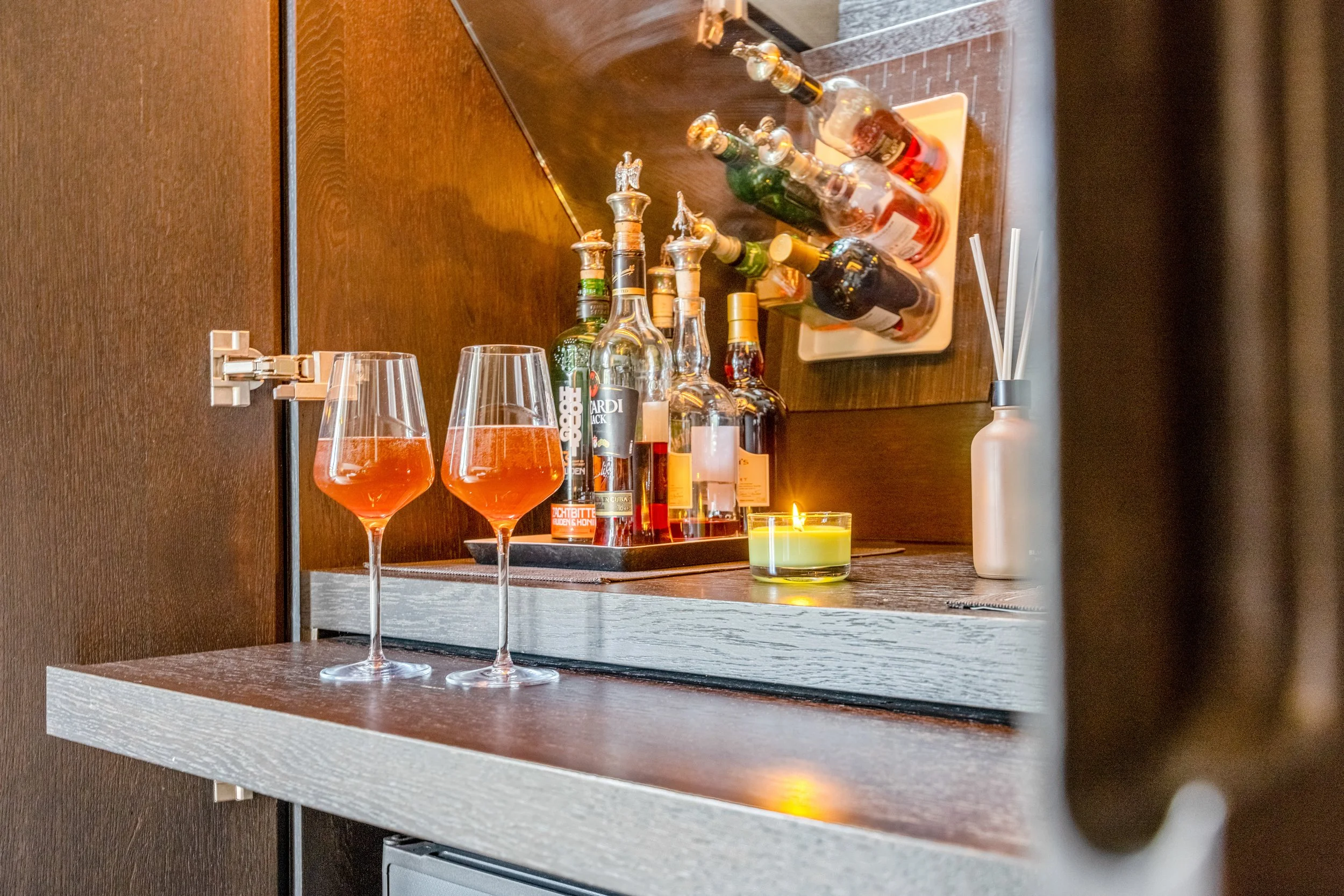Rum cocktails, verschillende soorten likeuren, een kaars en een diffuser op een donkere houten bar of tafel.