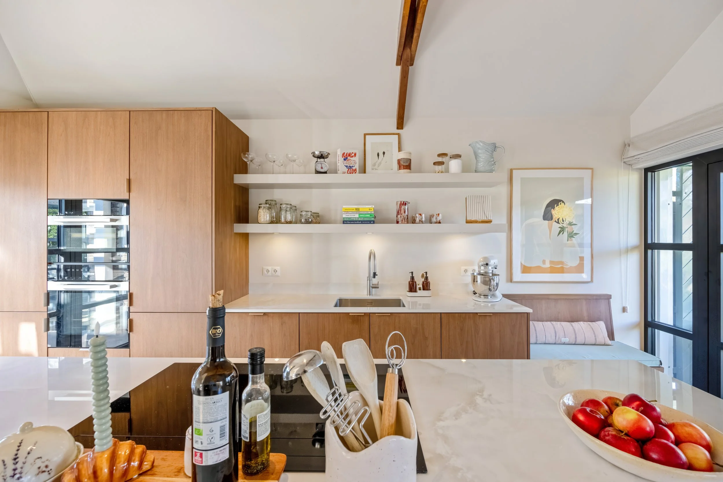 Modern keuken met witte en houten afwerking, open schappen met glas en keramiek, keukengerei en fruit op het aanrecht.