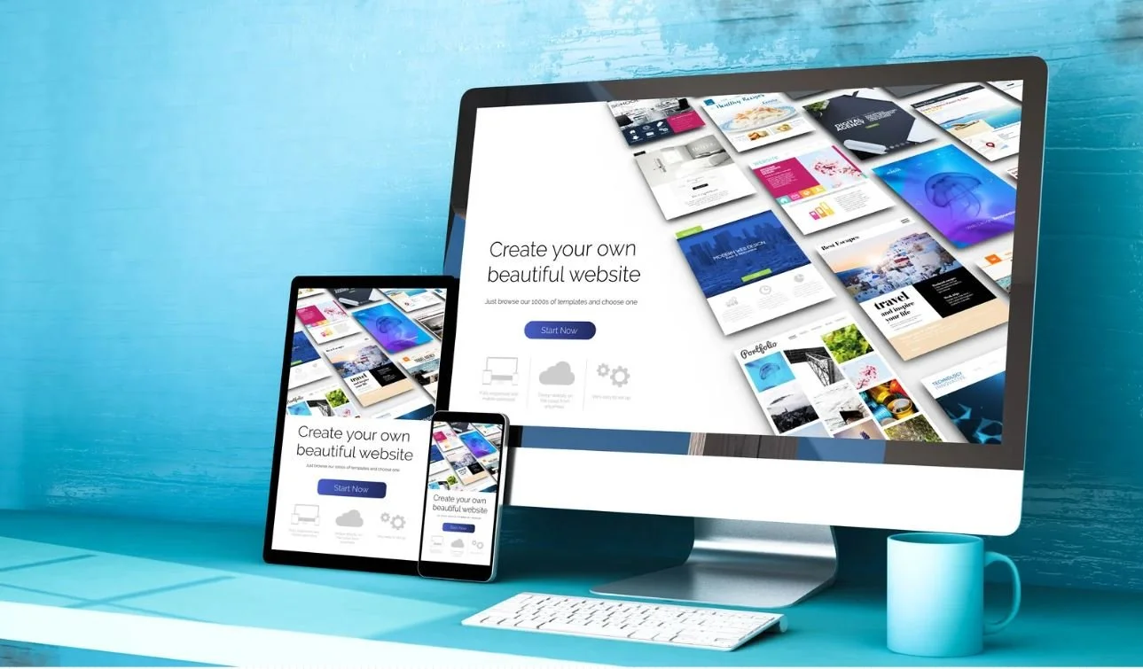 Computer monitor, tablet, and smartphone displaying a website builder with the text 'Create your own beautiful website' and a 'Start Now' button, on a teal desk with a keyboard and a mug.