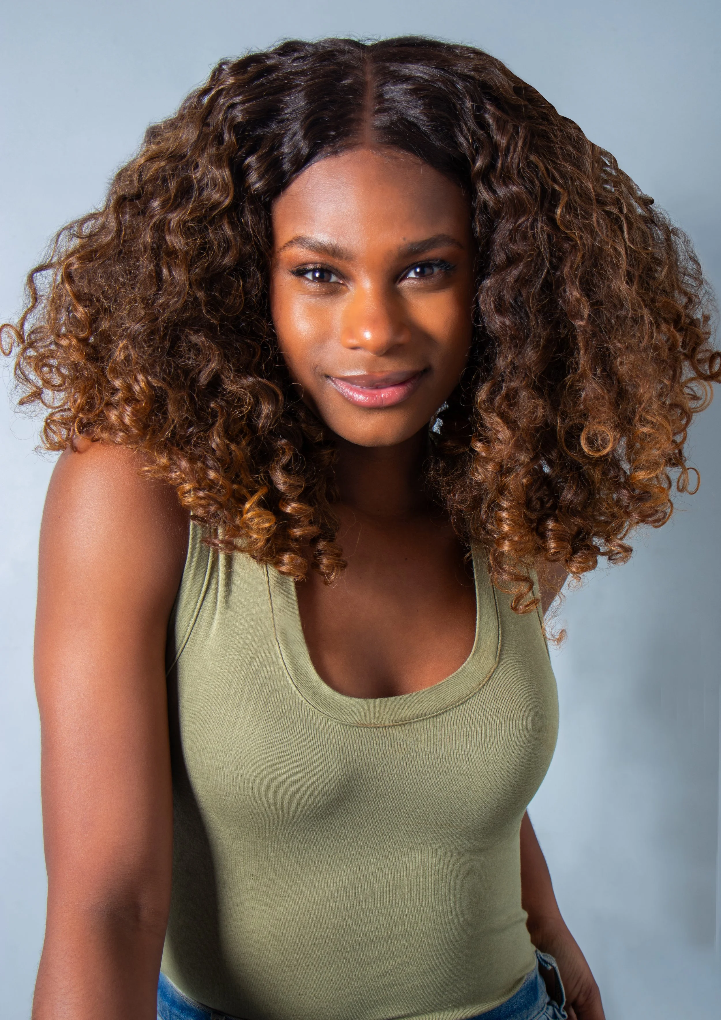 A woman with curly brown hair wearing a green sleeveless top and smiling.