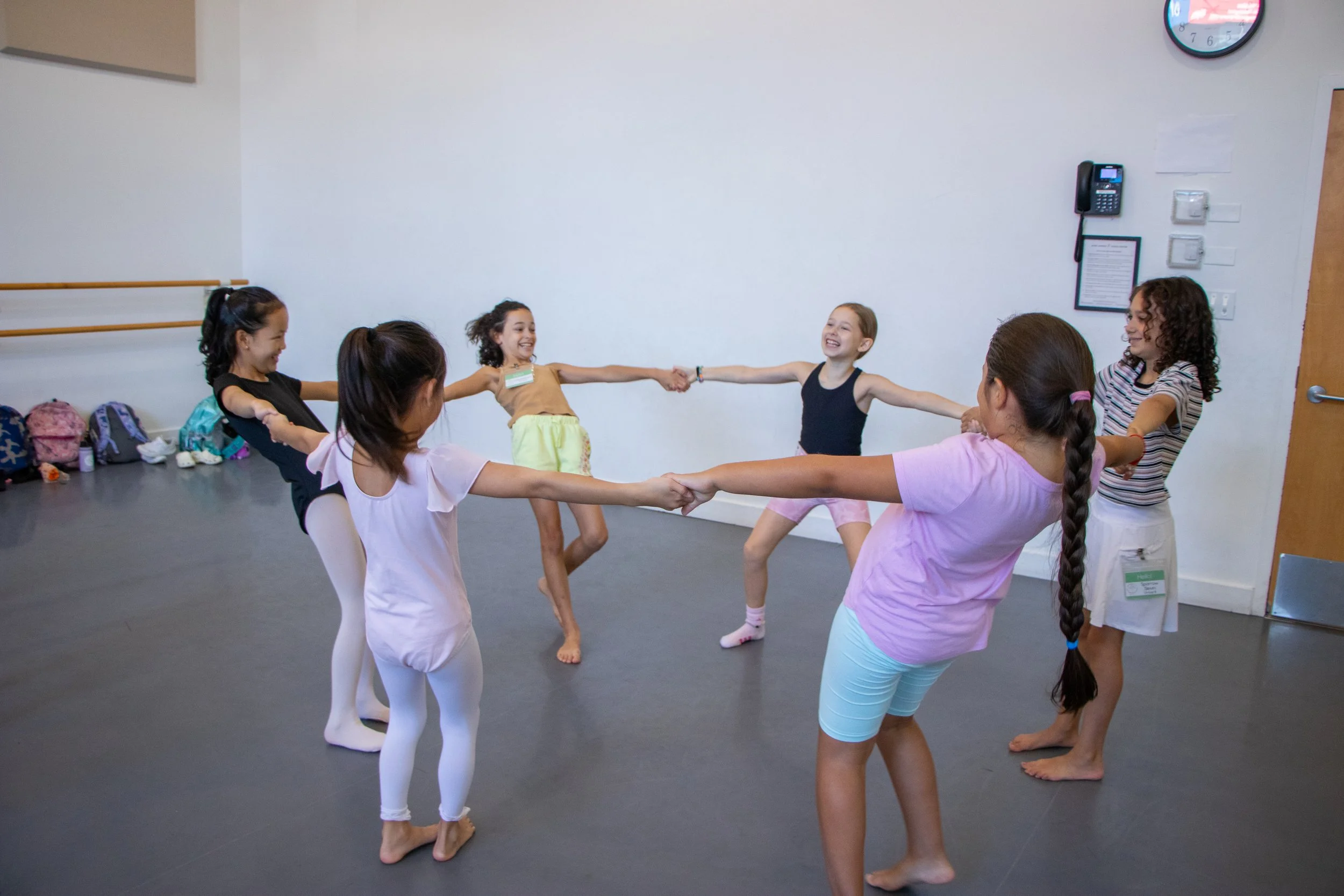 Six young girls holding hands and dancing in a circle indoors