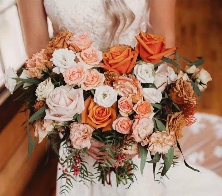 Bridal bouquet of orange, peach, white, and light pink roses and lisianthus with greenery.
