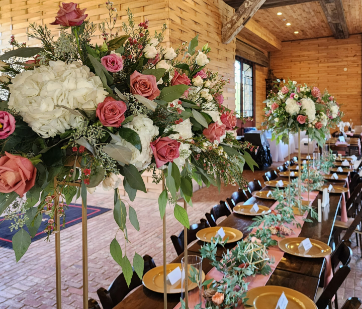 A long banquet table decorated with tall floral centerpieces featuring white hydrangeas, 'Cappuccino'  roses, and greenery.