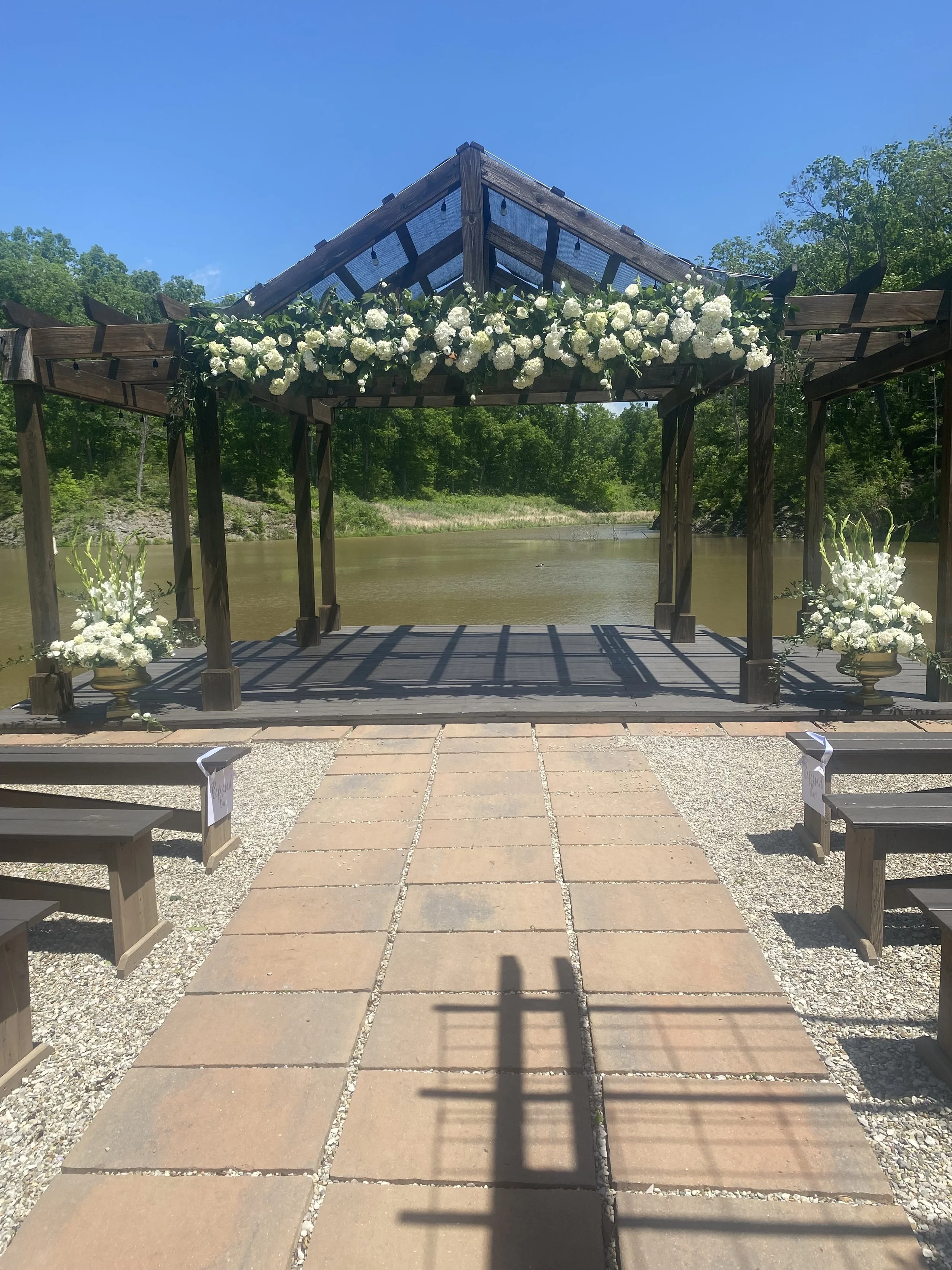 Outdoor wedding ceremony setup with a wooden arbor decorated with white hydrangeas, lisianthus, and gladiolus.