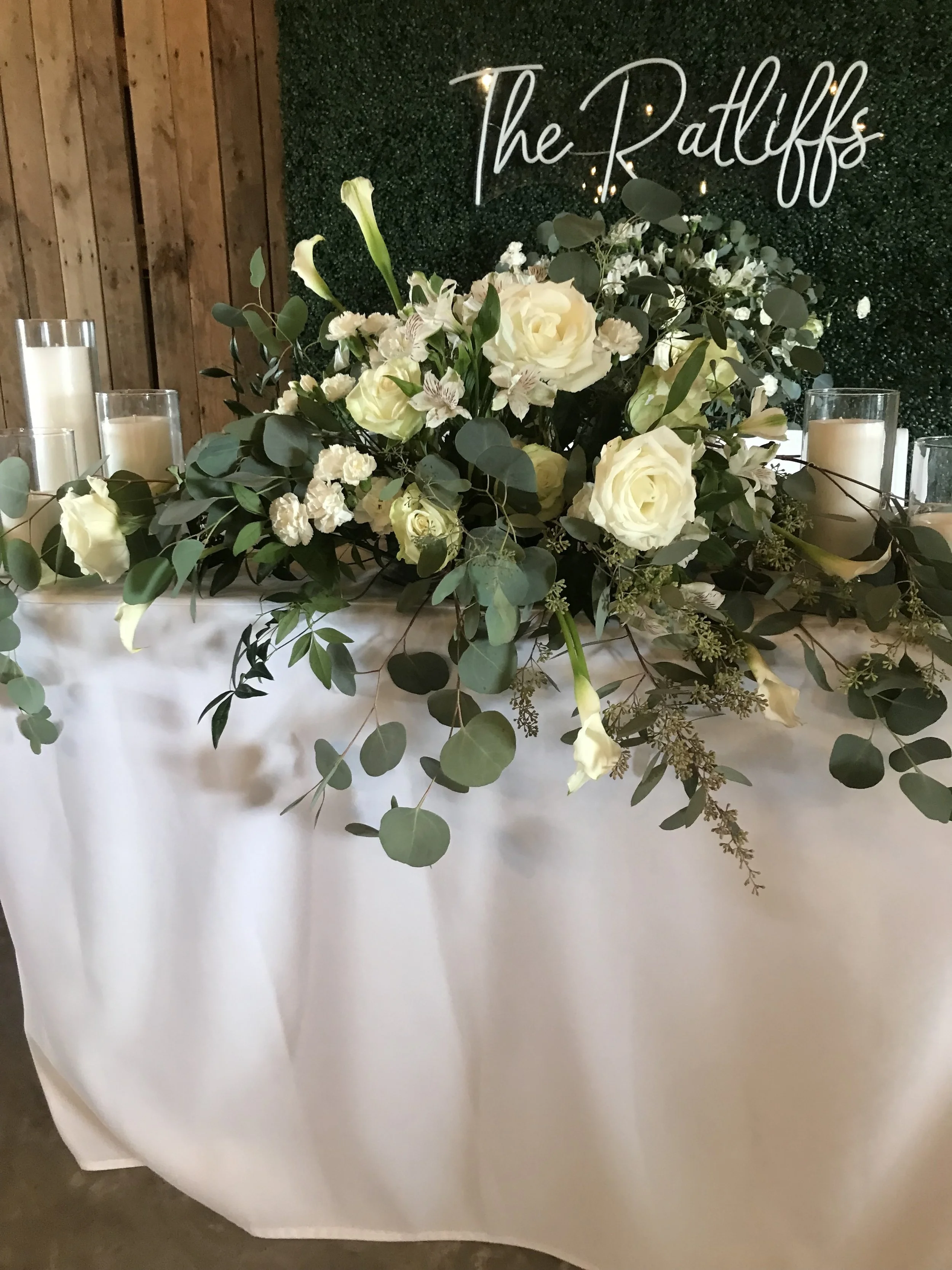 A floral arrangement with white roses and calla lilies, greenery on a welcome table. Reception flowers.