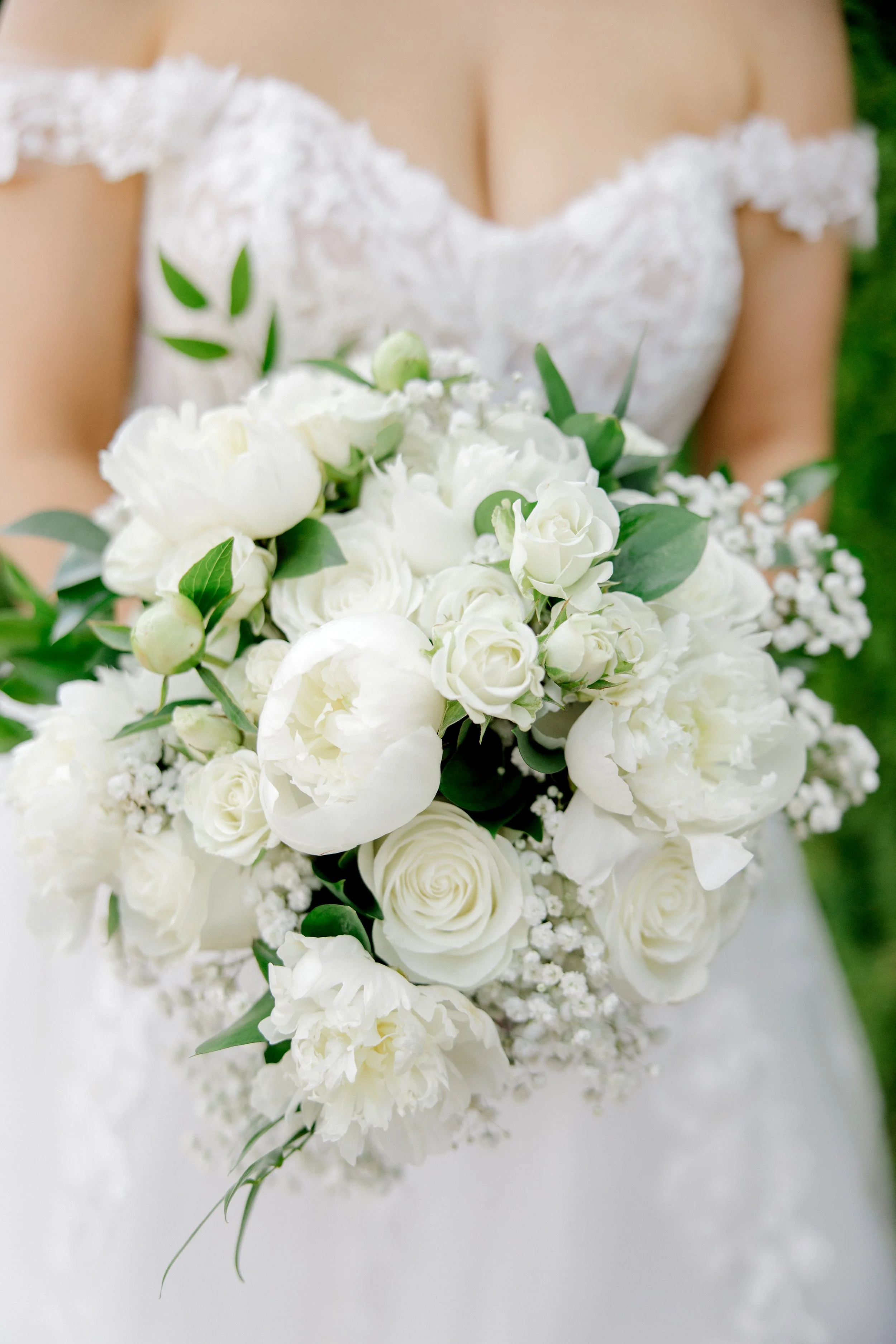 Hand tied bridal bouquet of white peonies, roses, and baby's breath.