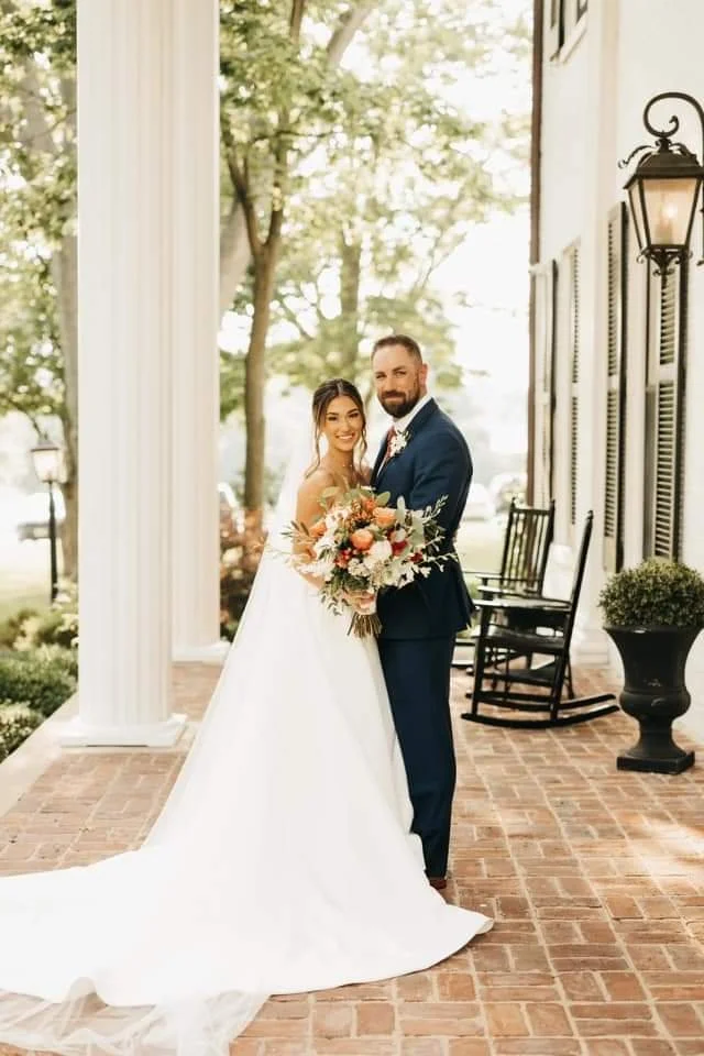 Bride carrying a hand tied bouquet of white dendrobium orchids, peach and tera cotta roses, hypericum berries.