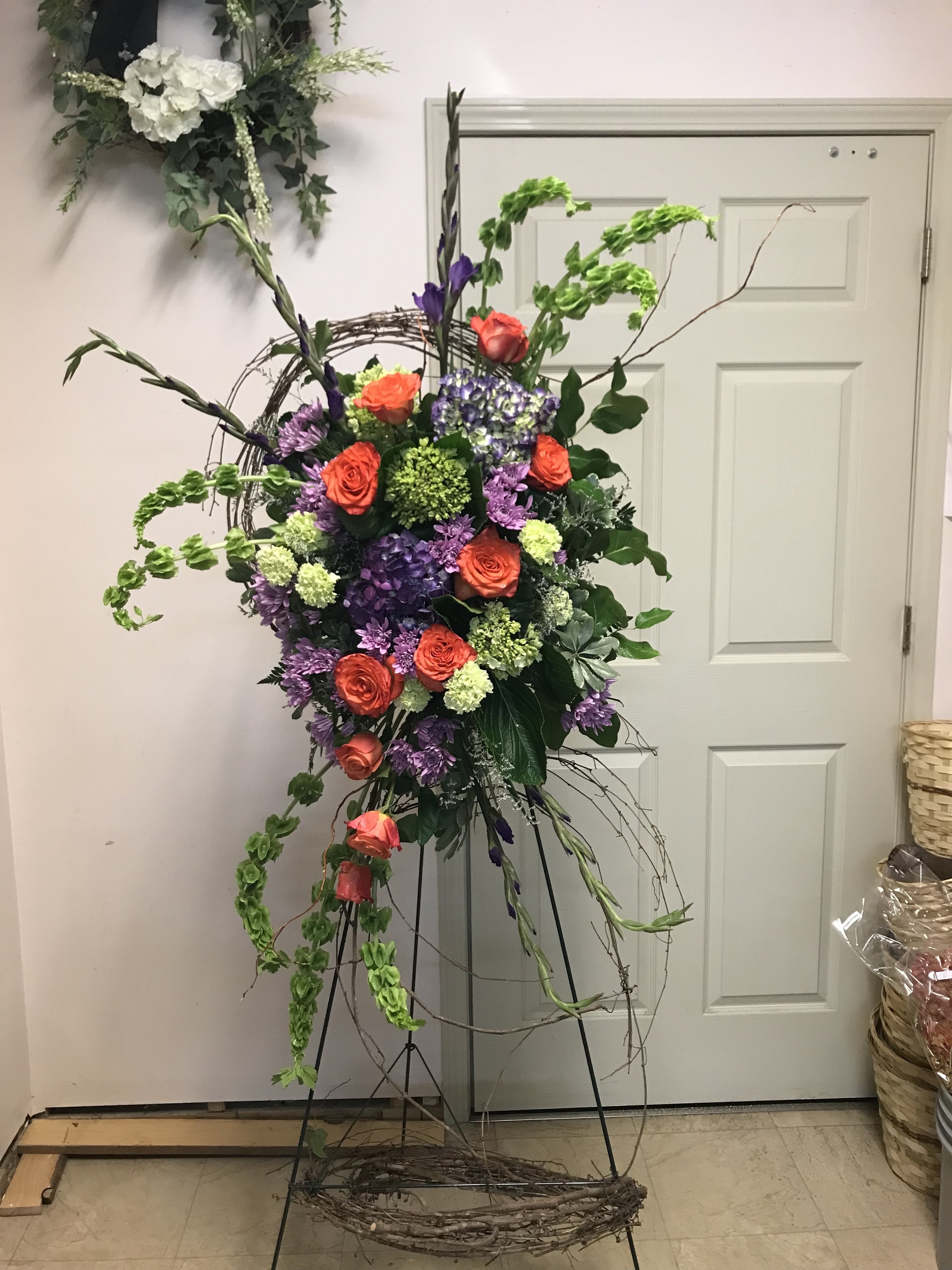 Colorful floral arrangements with roses, hydrangeas, and greenery on metal stand in front of a door.
