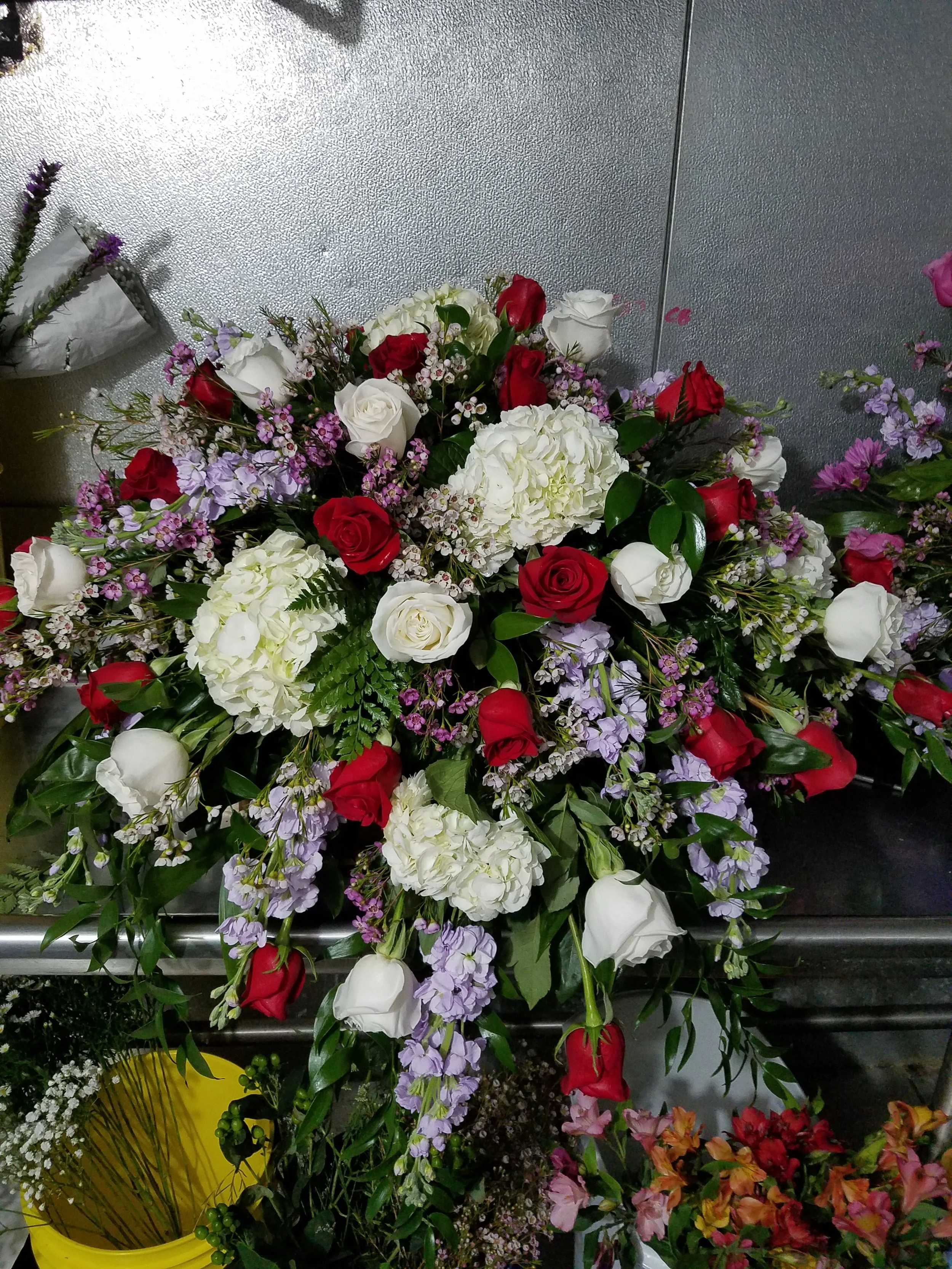A casket spray with red roses, white roses and hydrangeas, lavender stock, and purple wax flower.