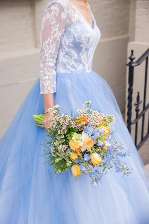 A woman in a light blue wedding dress with lace sleeves holding a colorful bouquet of flowers.