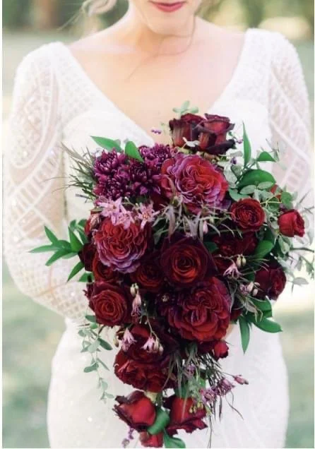 Cascading bouquet of dark red and purple flowers, including roses and other blooms.