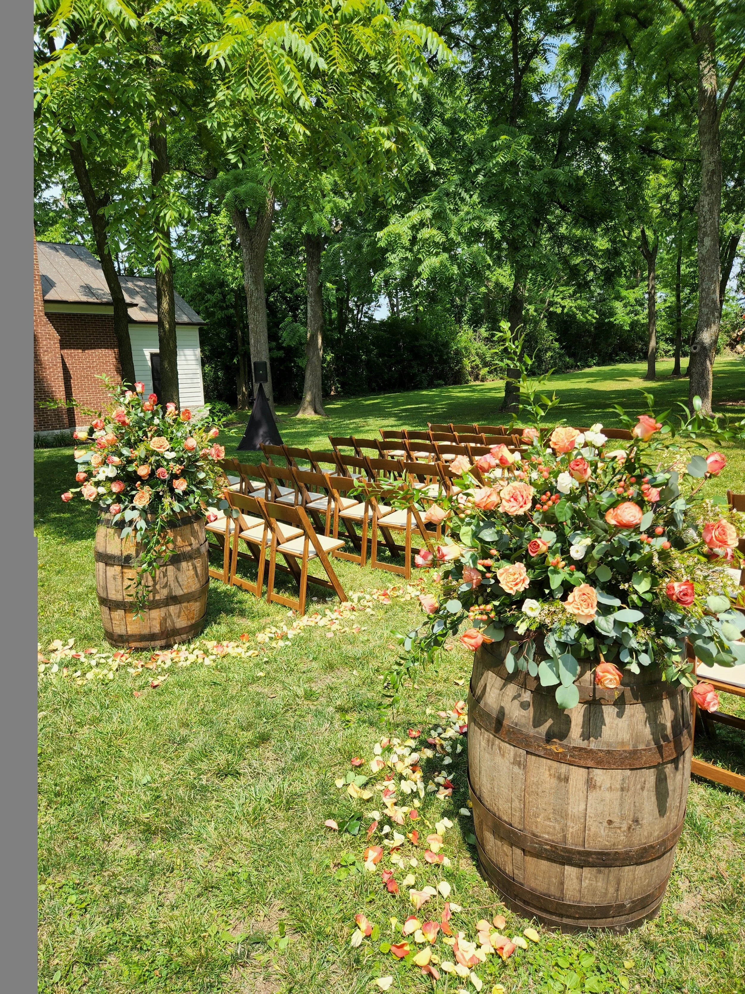 Outdoor wedding setup with aisle flowers. Arrangements set atop whiskey barrels at beginning of aisle.