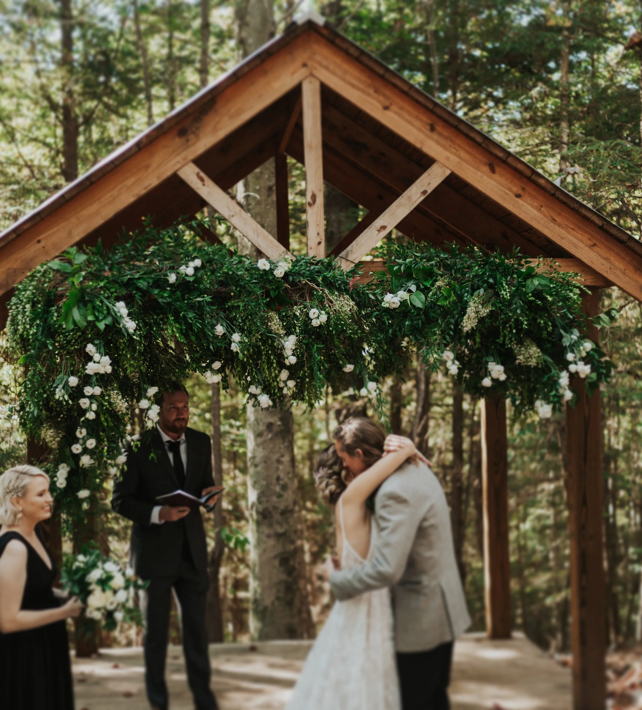 A wedding ceremony, with a wooden arch decorated with greenery and white flowers.