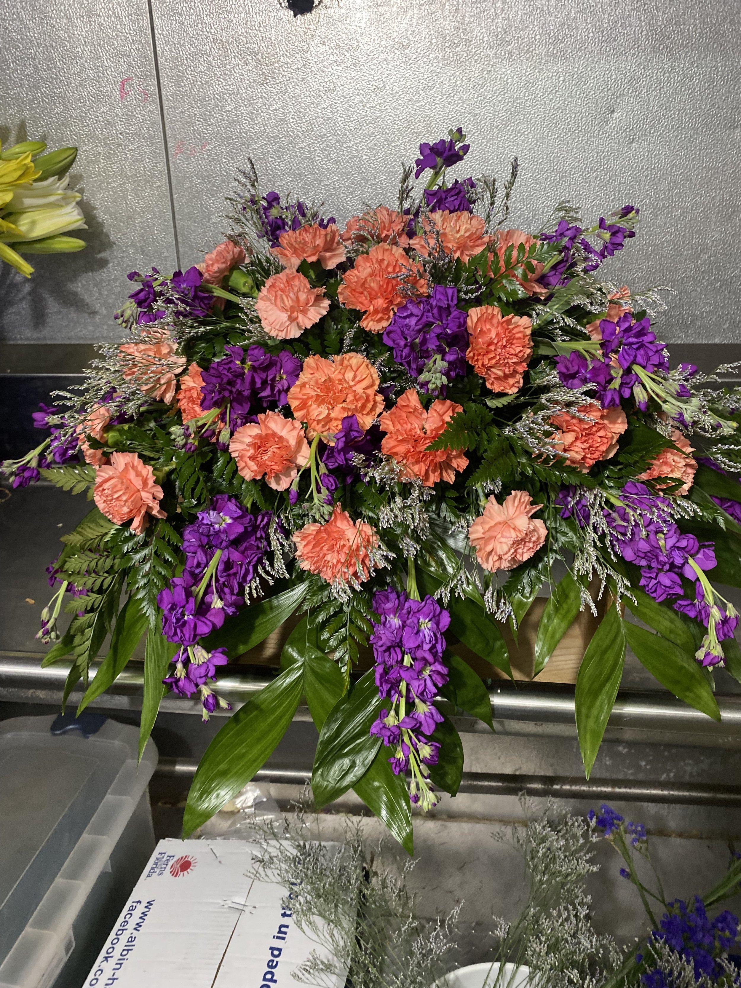 A vibrant casket spray with orange carnations and purple stock.