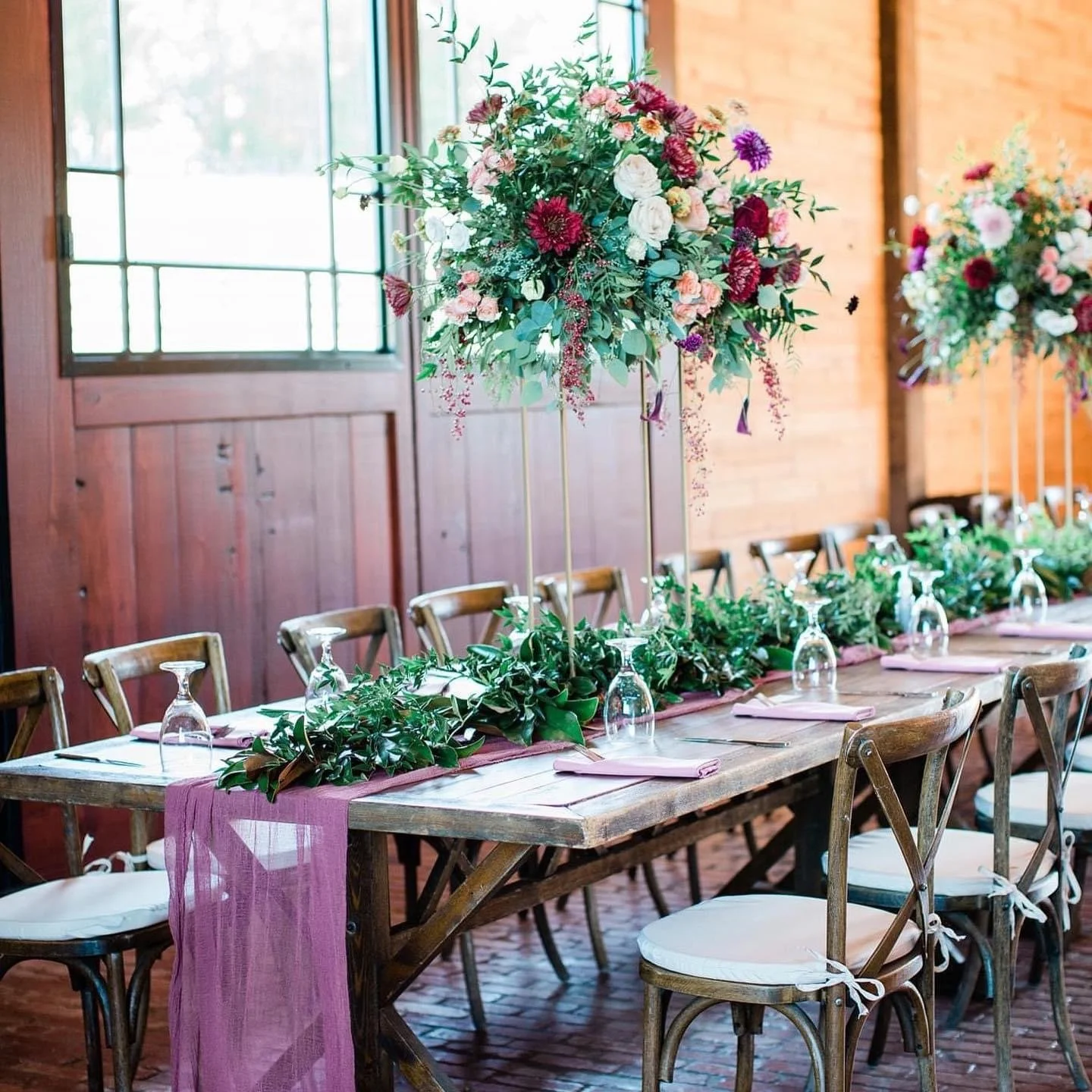 A decorated banquet table with floral centerpieces and table settings for an event or wedding in a rustic venue.