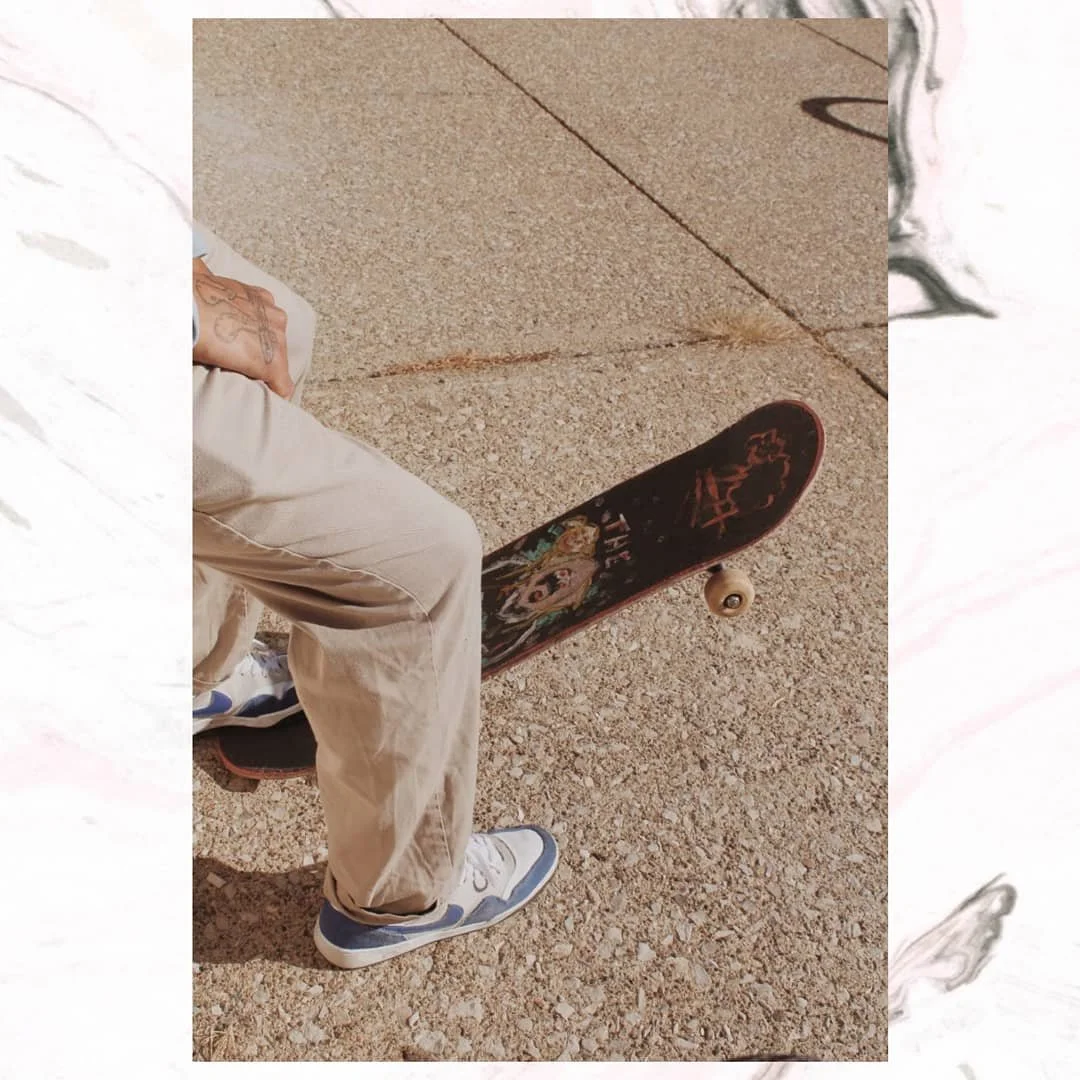 Person sitting on a curb with their skateboard on the ground nearby, wearing beige pants and sneakers.