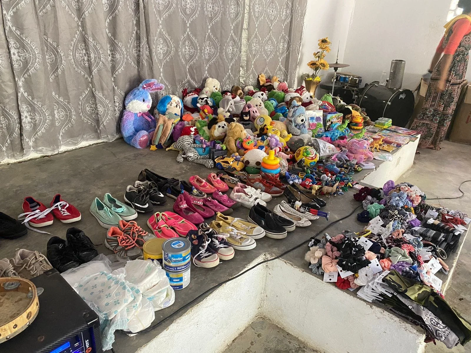 A wide variety of toys and shoes arranged on a white platform, with plush animals and children's shoes in the foreground and additional toys and accessories in the background.