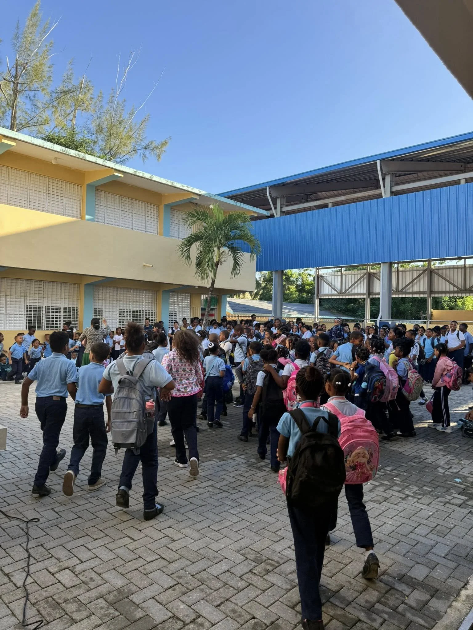 School children in uniform, carrying backpacks, walking outside school building.