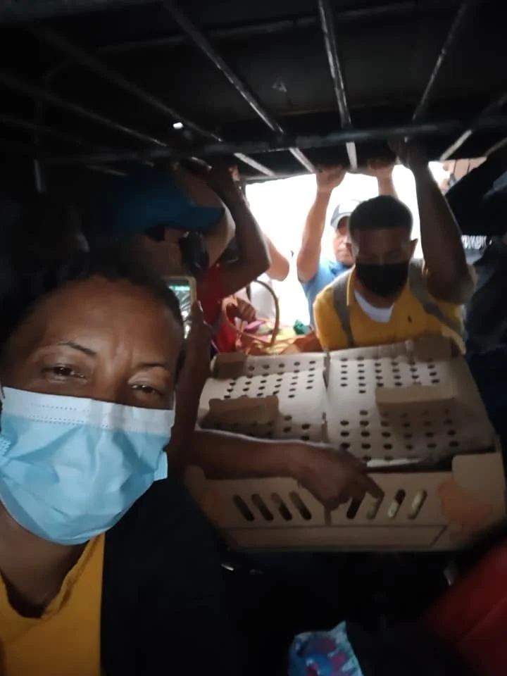 Group of people wearing face masks inside a crowded vehicle, with some appearing to be loading or unloading goods.