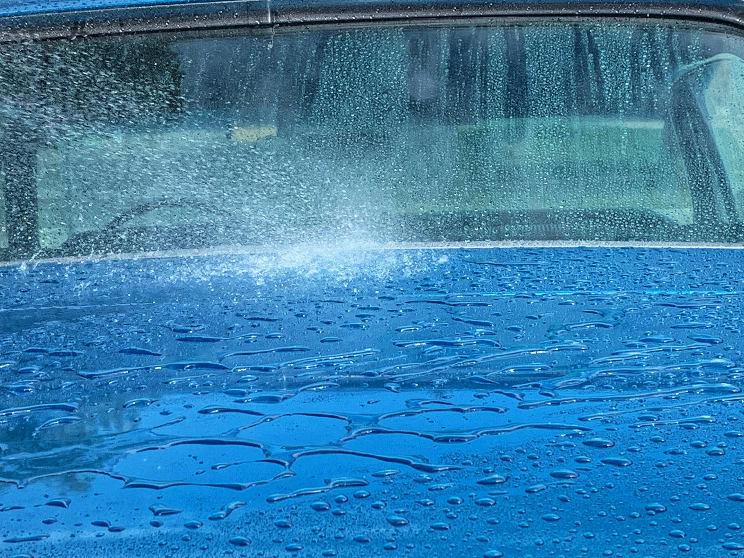 Regentropfen auf einer blauen Oberfläche vor einer regennassen Windschutzscheibe