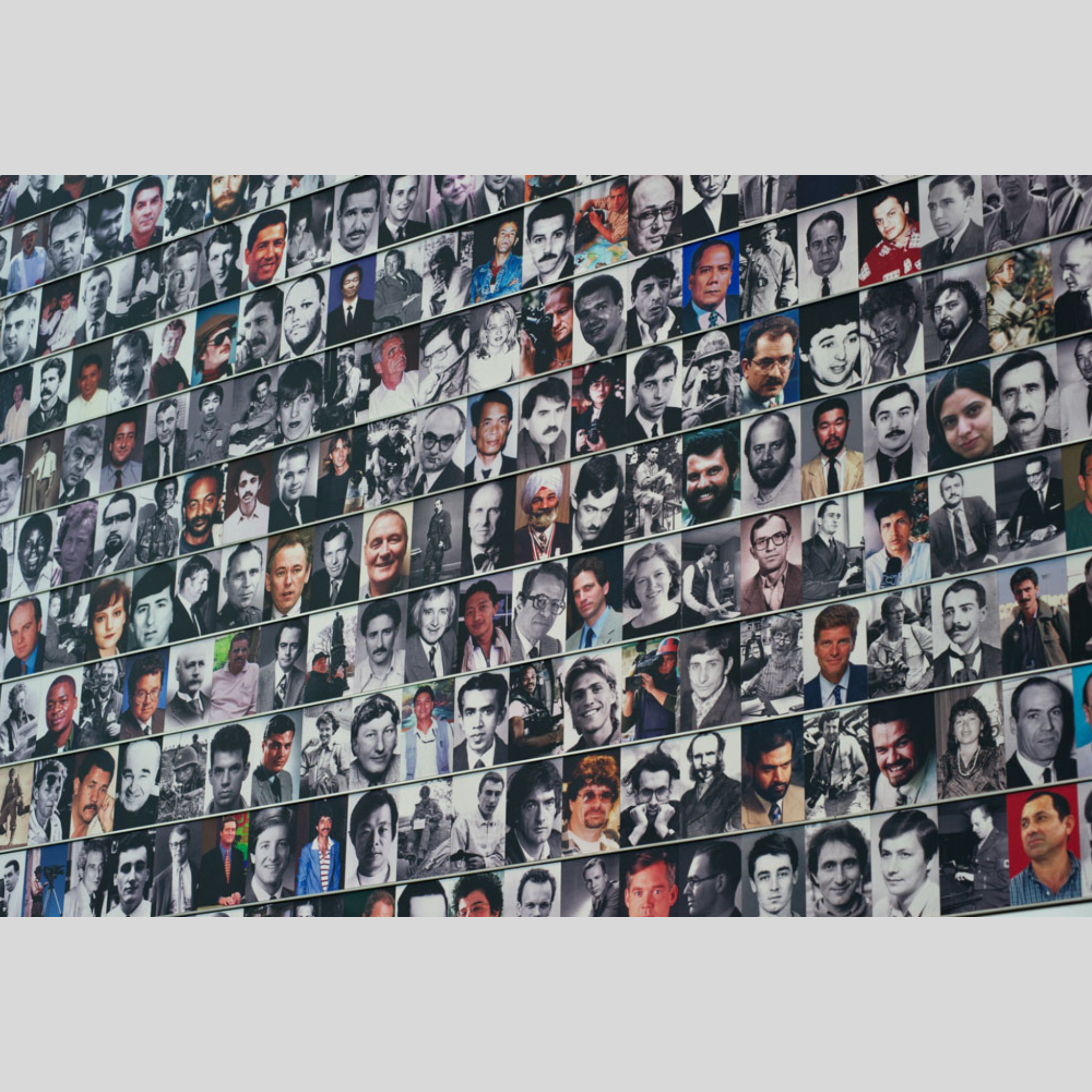 Un mur recouvert de nombreuses photos de personnes, en majorité en noir et blanc. Certaines photos sont en couleur. La disposition est en rangées horizontales.