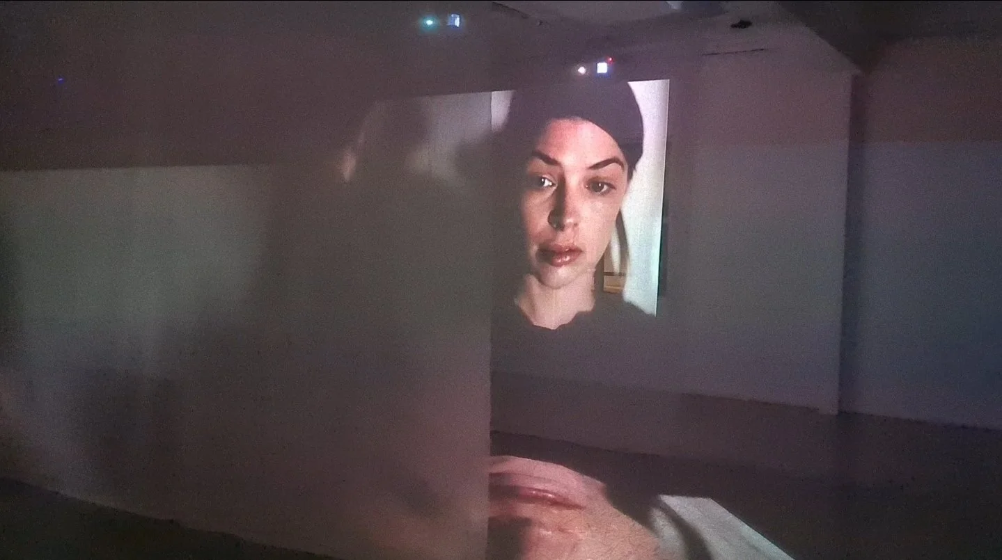 Projection d'une vidéo d'une femme avec des cheveux noirs foncés et un maquillage naturel sur un mur dans une pièce sombre.