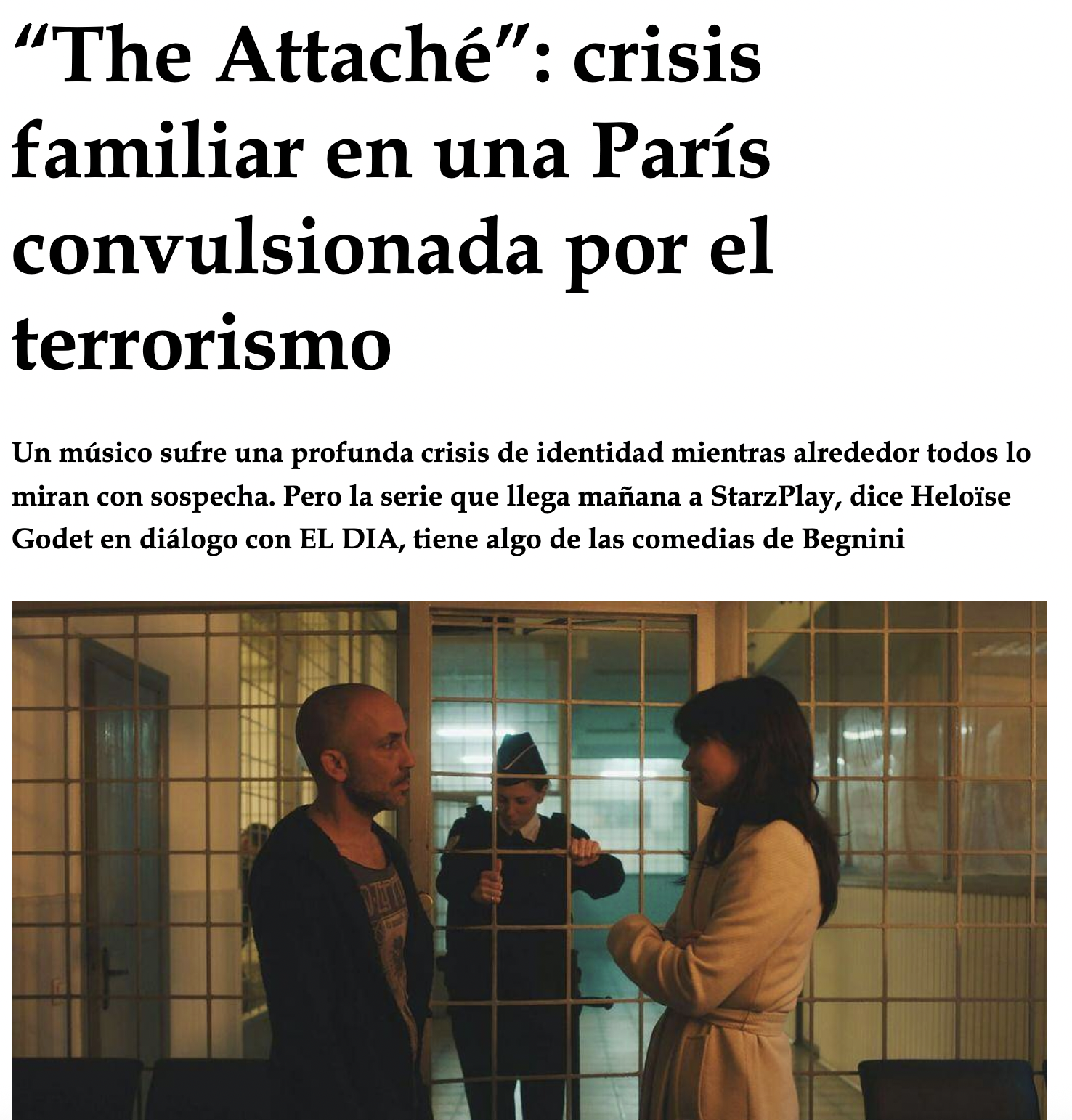 Deux femmes et un homme devant une grille de prison. La femme à gauche a les cheveux courts, porte un blazer et parle à la femme à droite qui a de longs cheveux et porte un manteau beige. Un homme en uniforme de garde se tient derrière la grille, reg