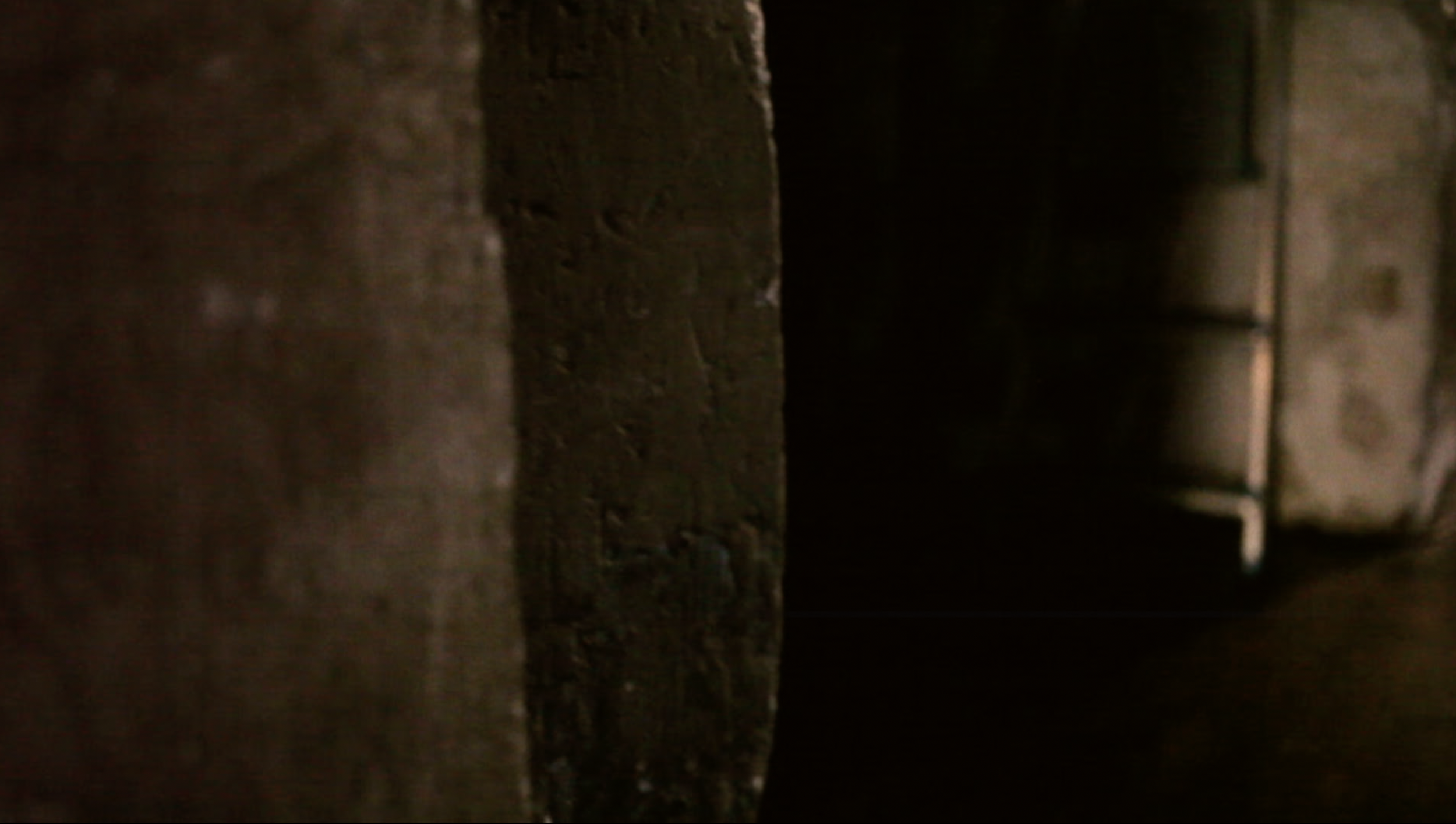 Une obscurité partielle avec un mur en pierre visible à gauche et un espace vide ou une zone sombre à droite.