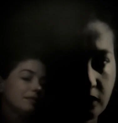 Une image sombre montrant deux visages, l'un féminin et l'autre masculin, dans une lumière faible.