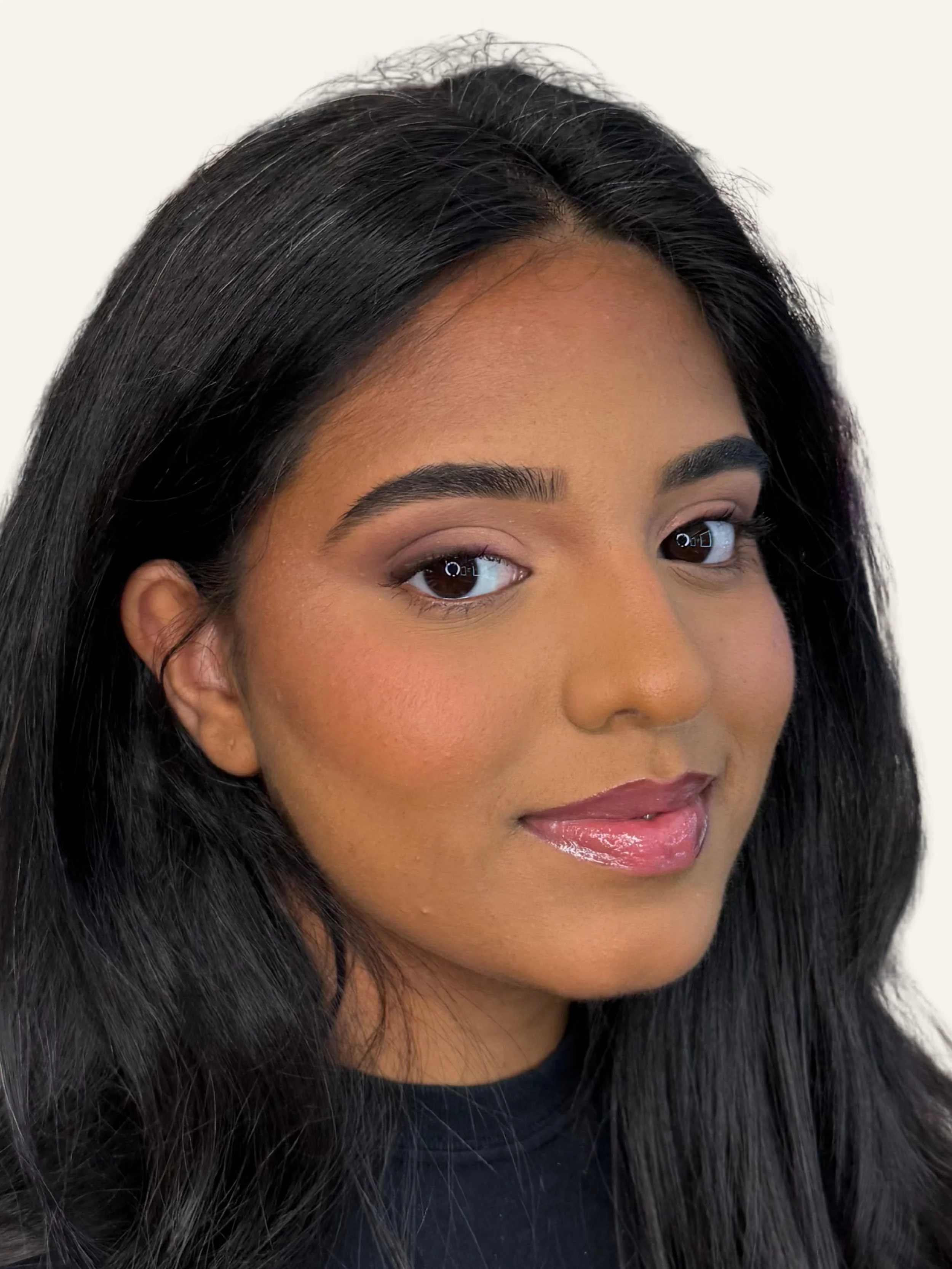 Close-up of a woman with long black hair, wearing makeup, and a black top, against a plain background.