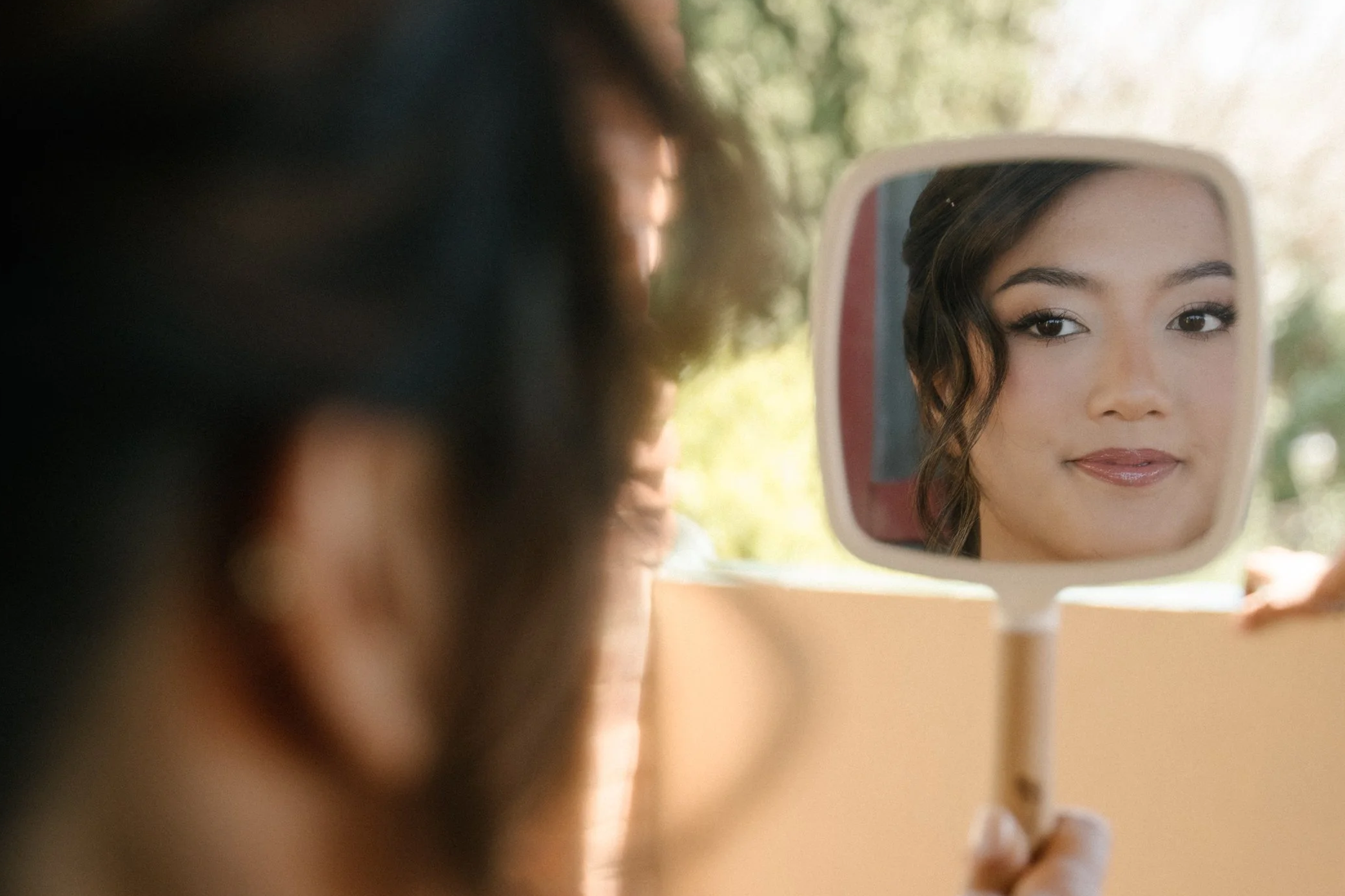 A woman looking into a mirror, showing her reflection with makeup and hairstyle.