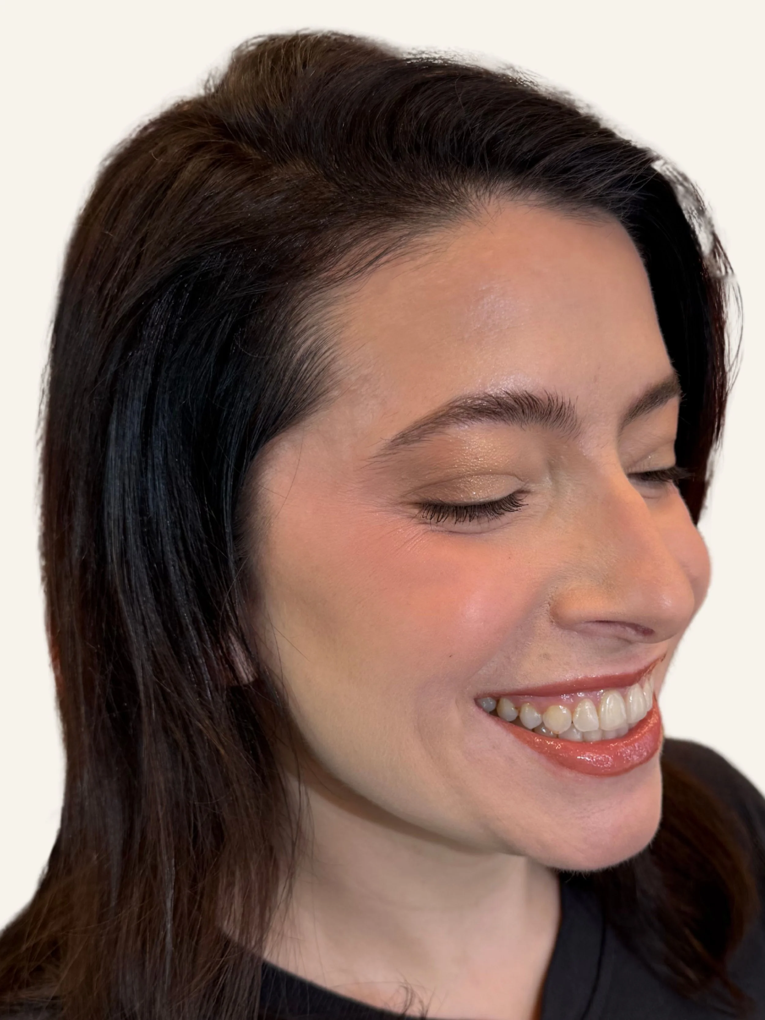 Close-up of a woman smiling with eyes closed, showing her teeth, dark hair, and light makeup.