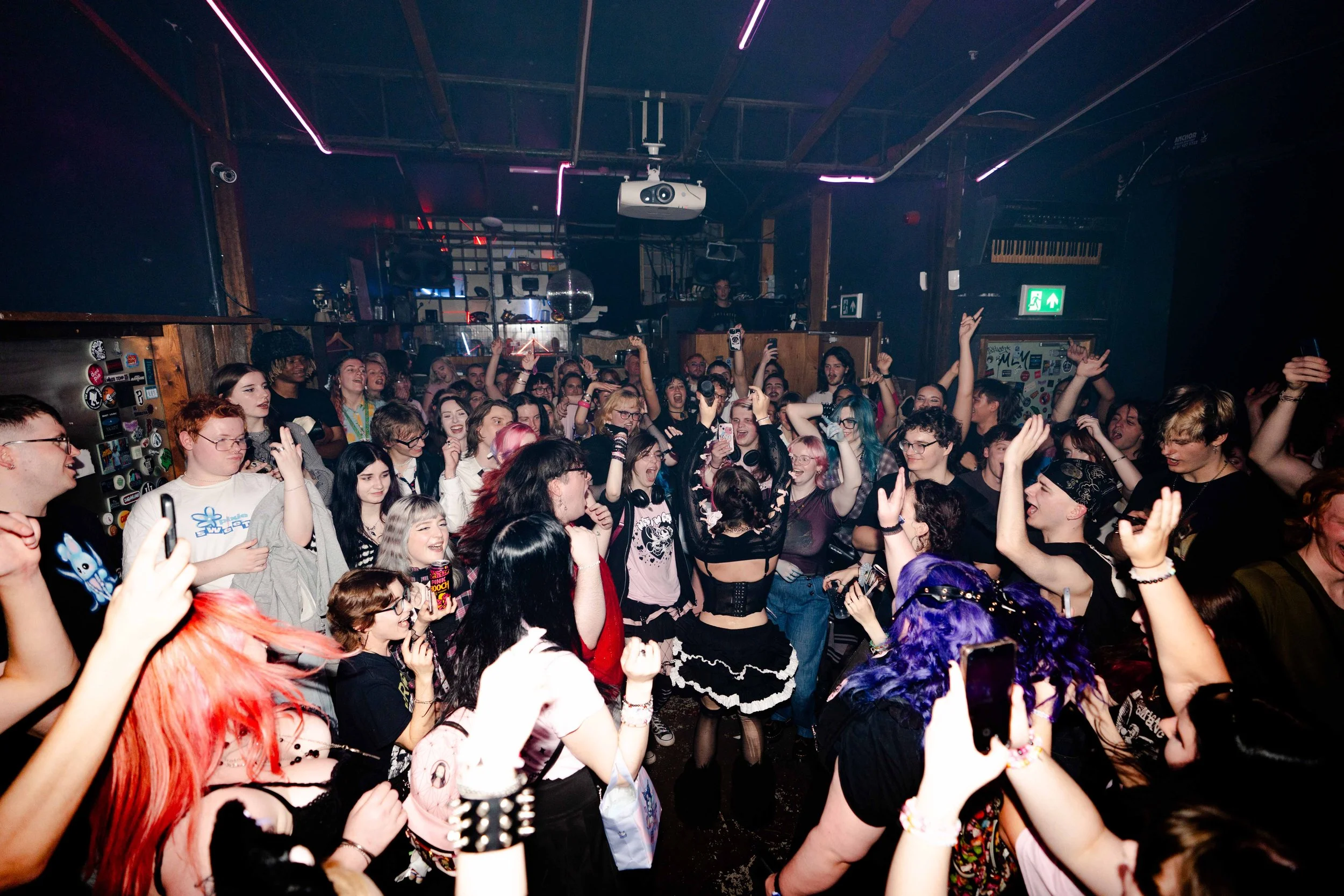 A lively crowd of young people dancing and enjoying music at a nightclub under colorful lighting.