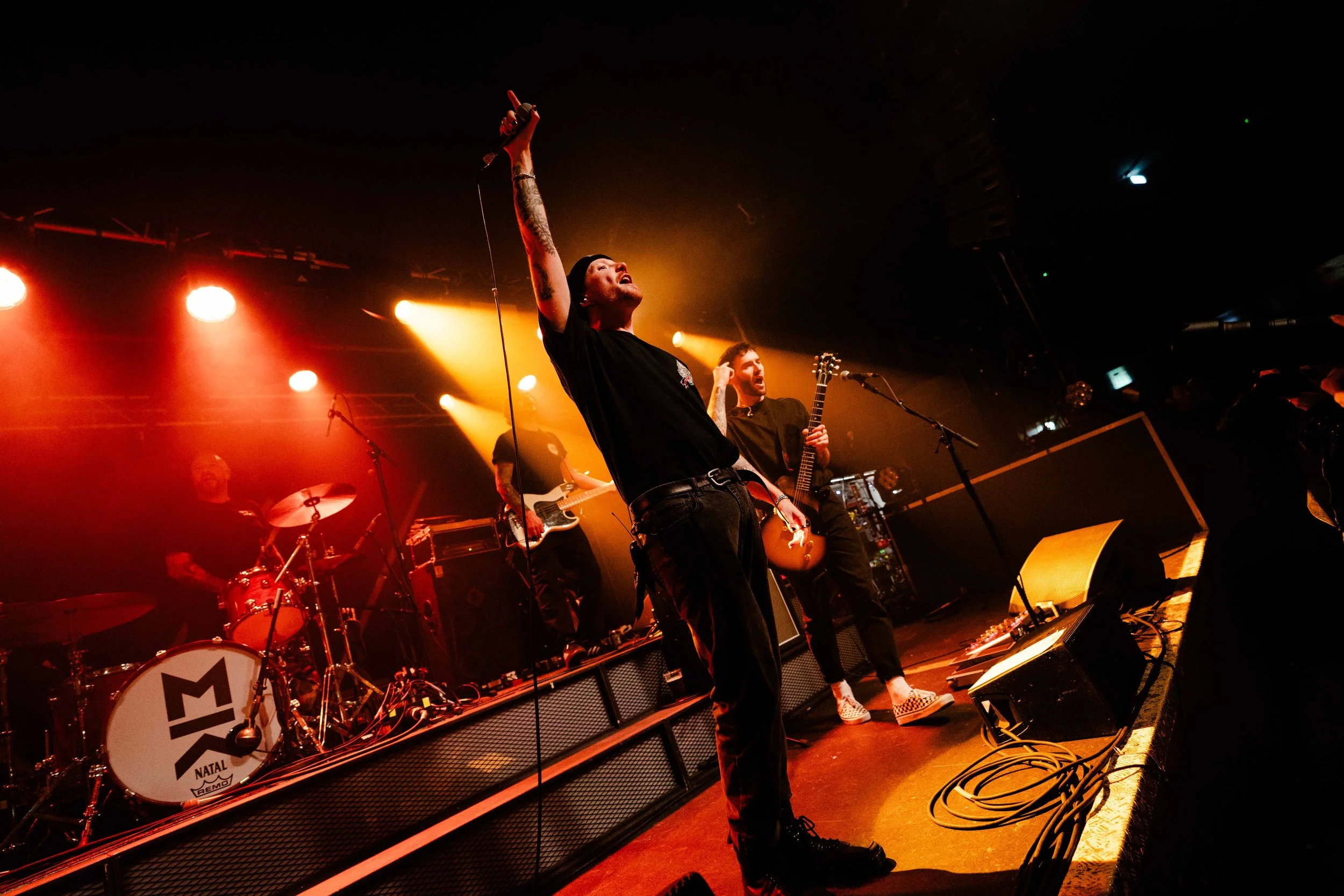 A band performing live on stage, with a lead singer holding a microphone up and singing, illuminated by colorful stage lights.