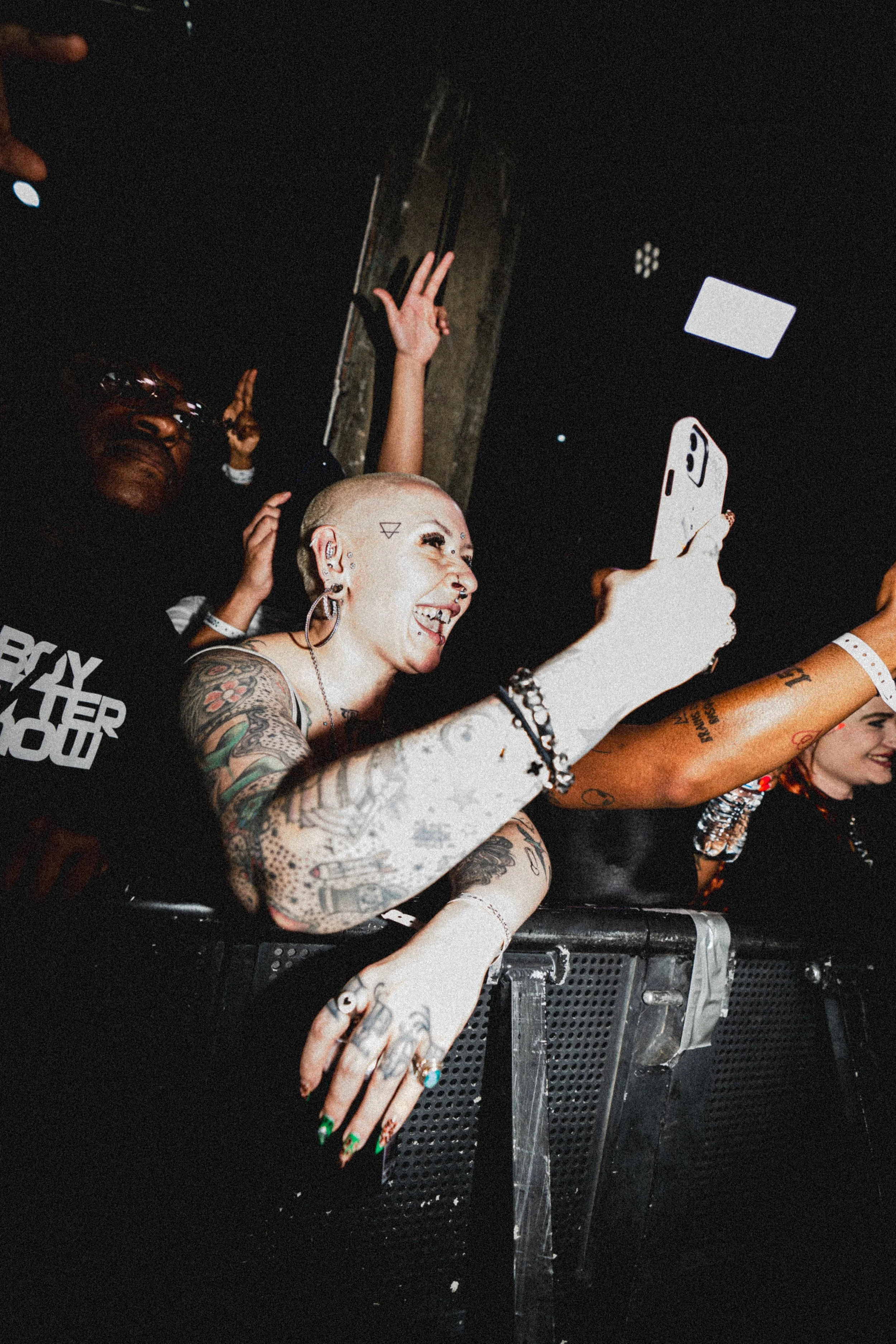 People at a concert or event, with one woman taking a selfie while others are dancing and enjoying themselves.