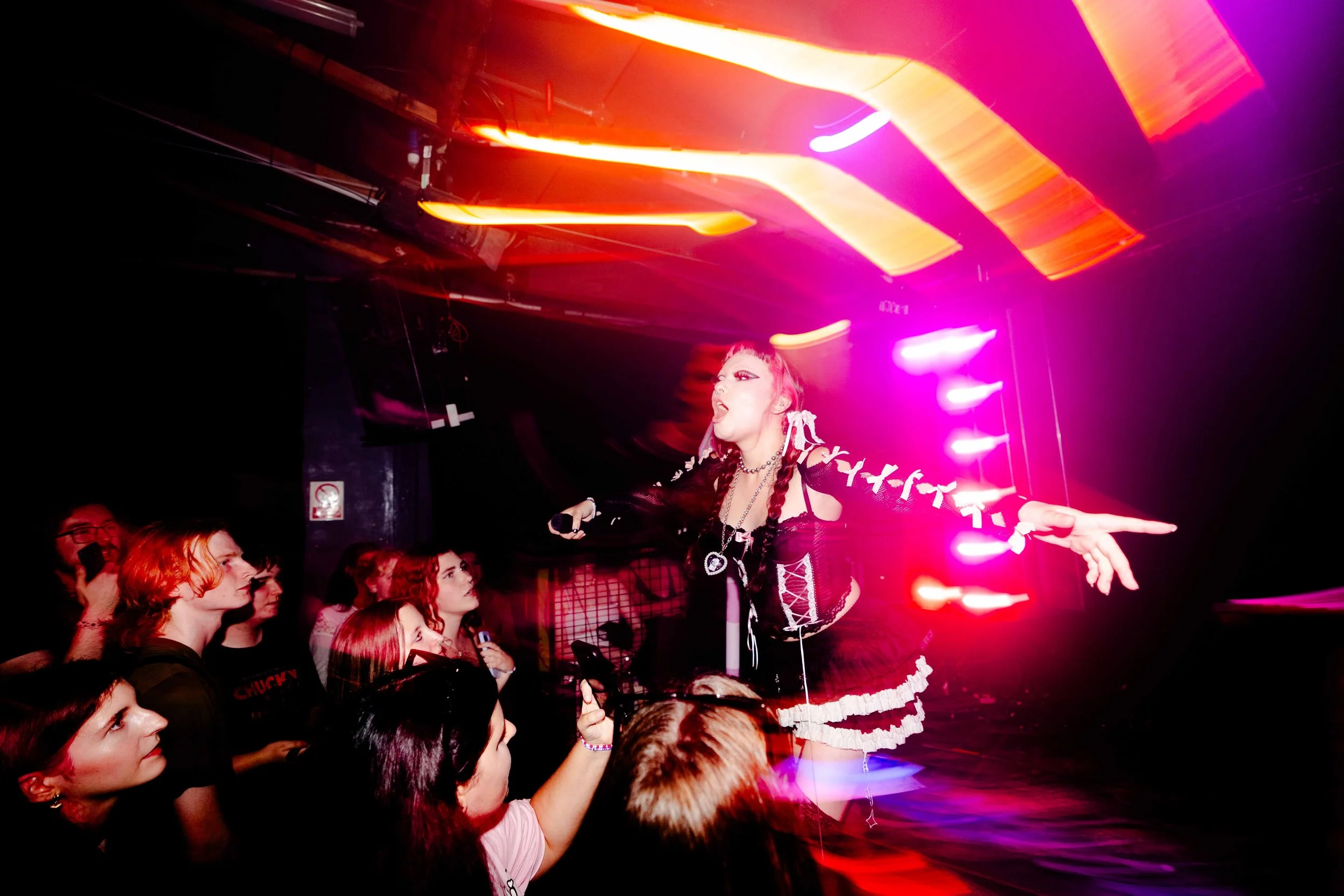 A performer on stage with bright pink, purple, and orange lights, engaging with an audience at a concert or event.