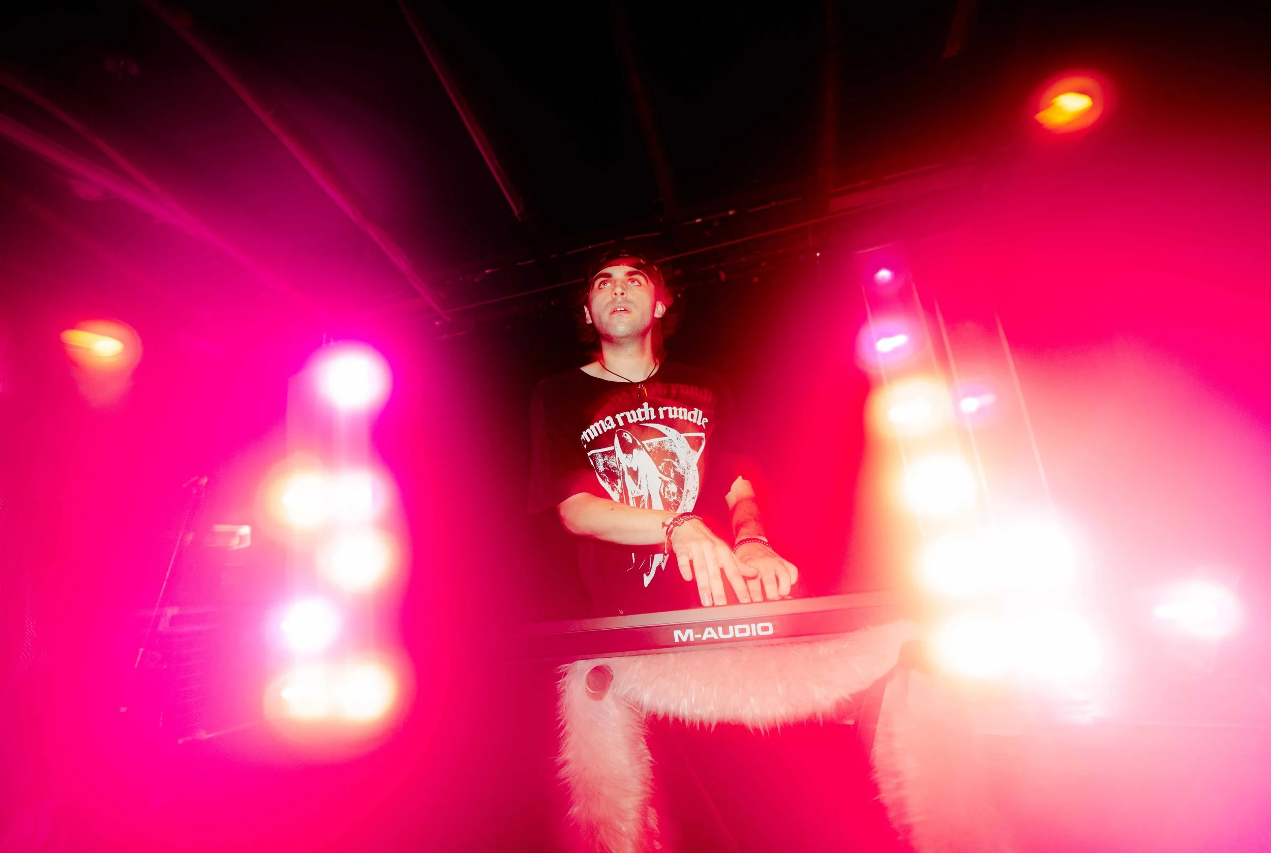 A DJ performs on stage with colorful pink and orange lighting.