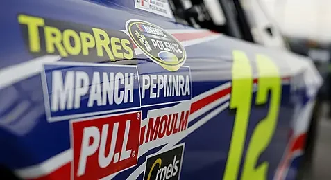 Close-up of a racing car with sponsor stickers including TropRes, IMPANCH, PULL, and others, featuring the number 12.