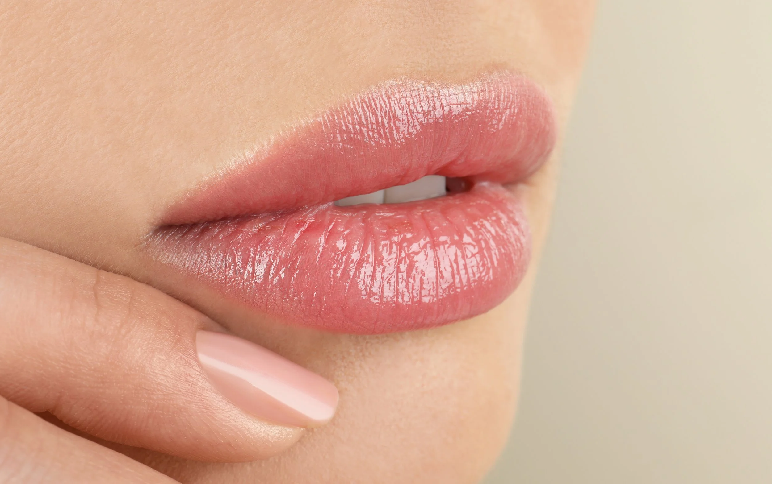 Close-up of a person's lips with light pink glossy lipstick, and a finger gently pressing the lower lip.