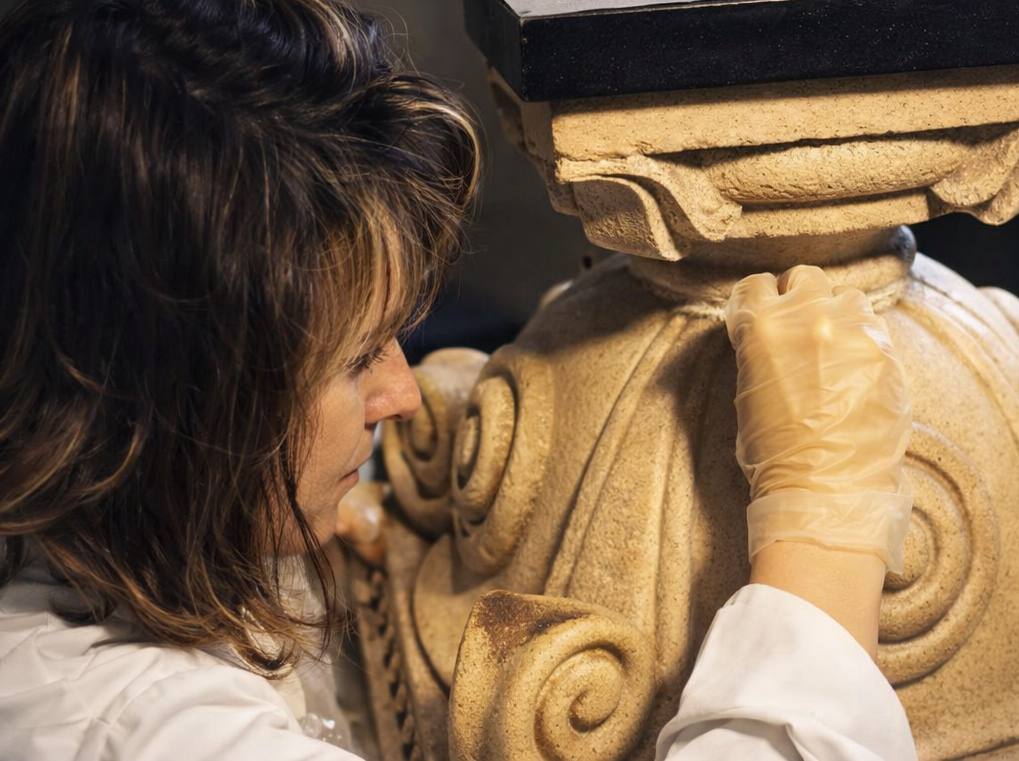 Restauro di una decorazione scolpita in pietra da parte di un'artista, indossa guanti e si concentra sulla scultura.