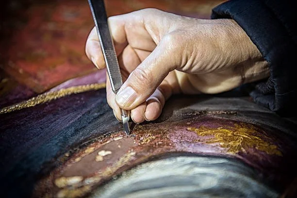 Una mano con guanto che utilizza uno strumento per restaurare o dipingere un quadro antico