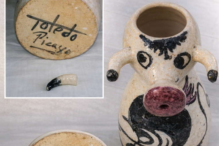 Una pignatta decorata a forma di maialino con un foro sulla parte superiore, con una decorazione artistica e un pezzo rotto. Sul fondo, una base con firma e data.