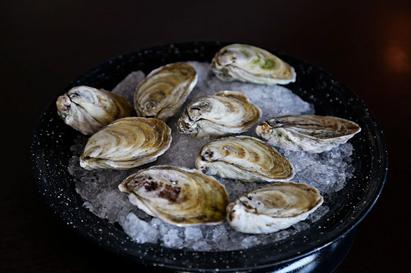 A black bowl filled with ice and oysters on top.
